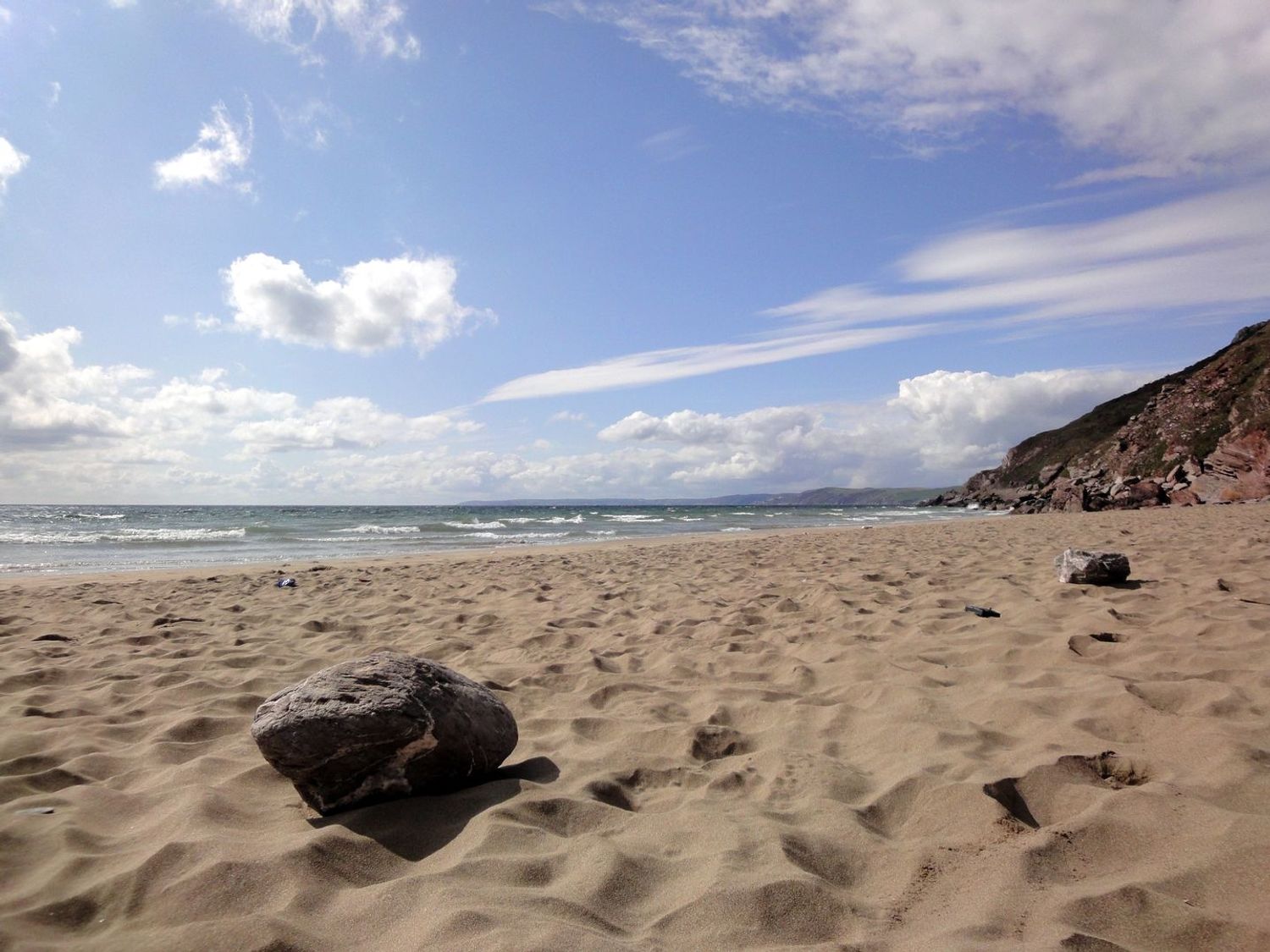 A sandy beach with rocks near the shoreline and hills in the background at Seagulls Nest in Whitsand Bay near Millbrook