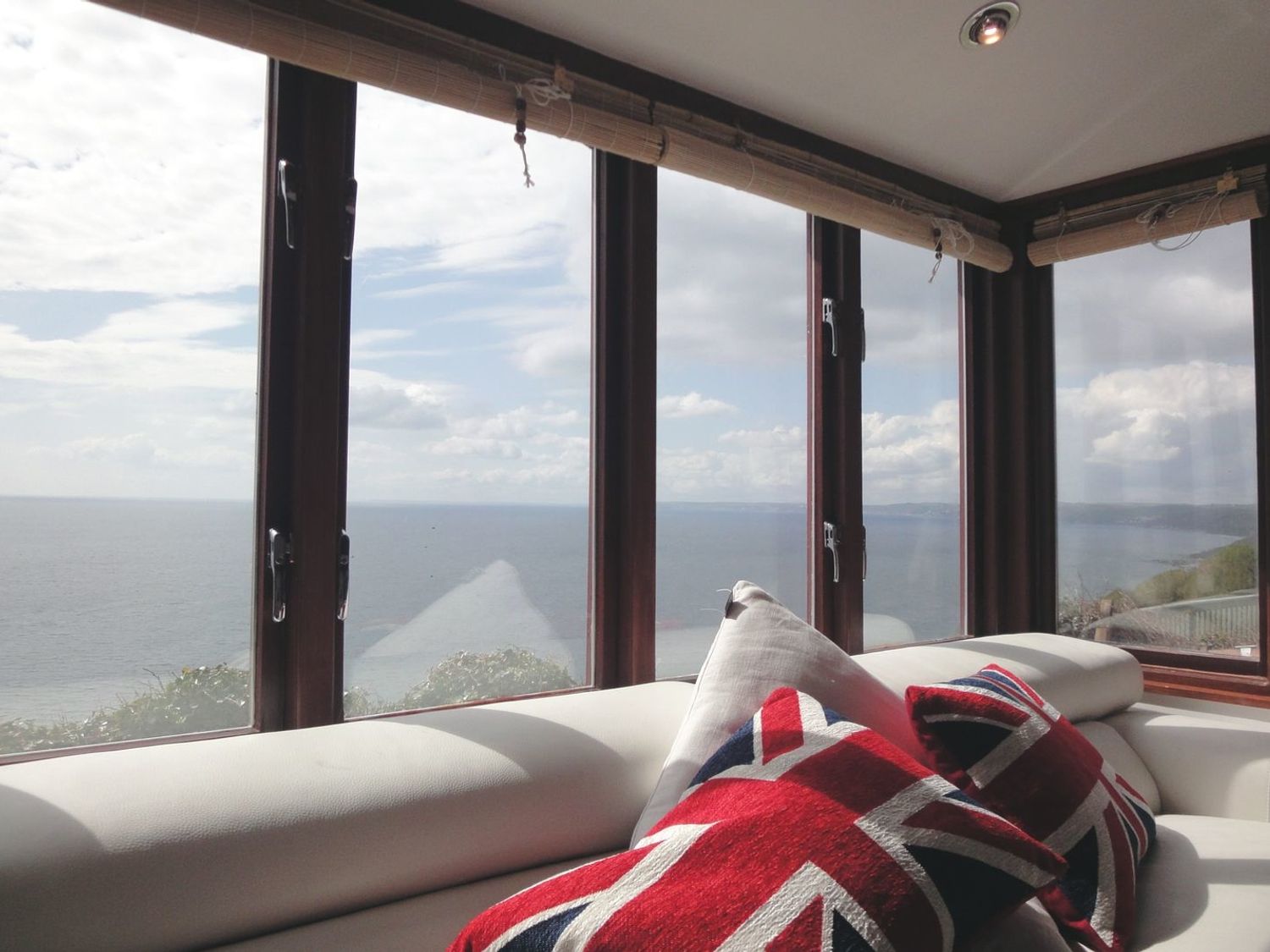 A seating area with Union Jack cushions by large windows overlooking the ocean at Seagulls Nest Whitsand Bay near Millbrook