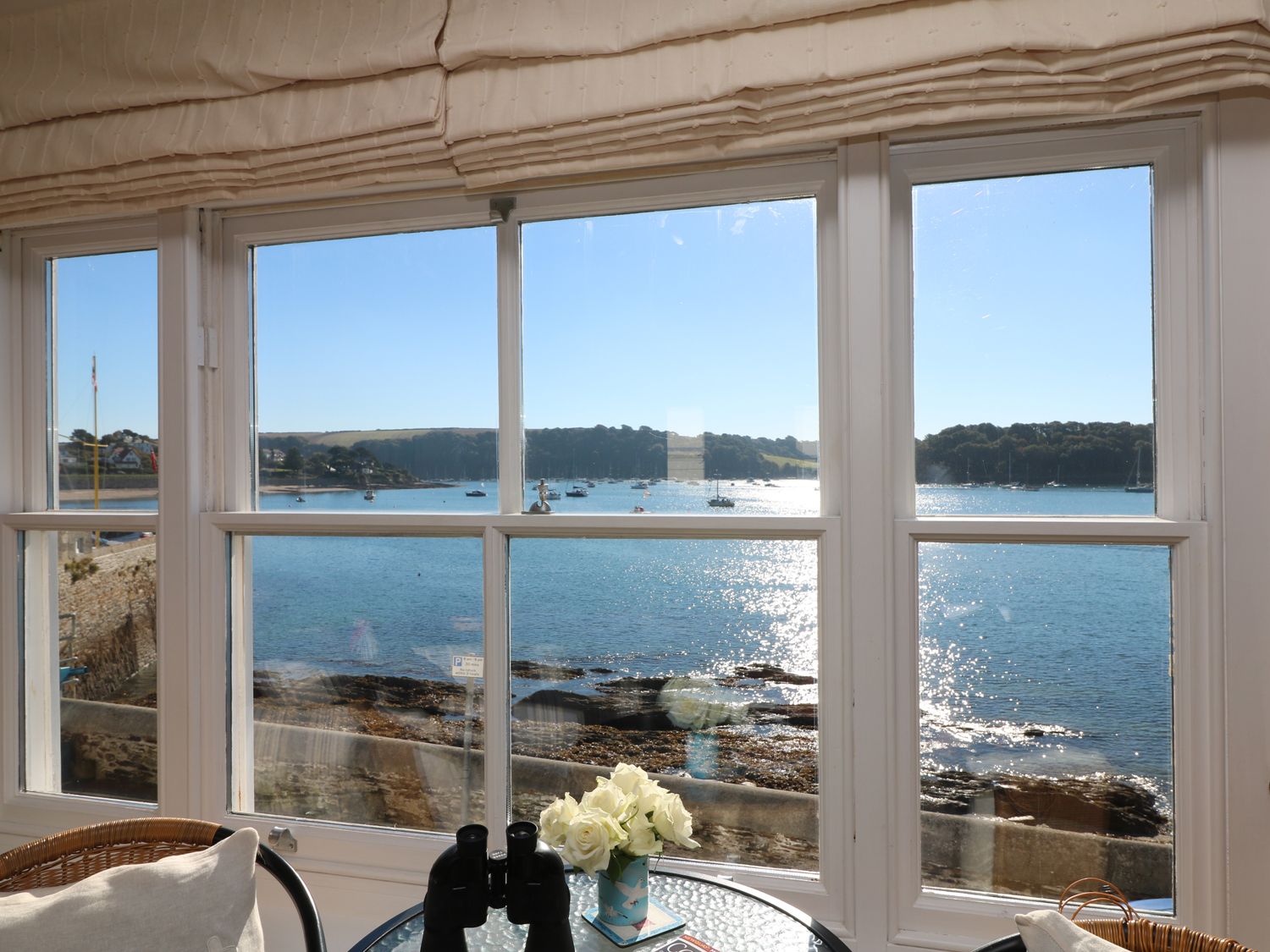 A window view overlooking a bay with boats on the water and hills in the background at Pier Cottage in St Mawes