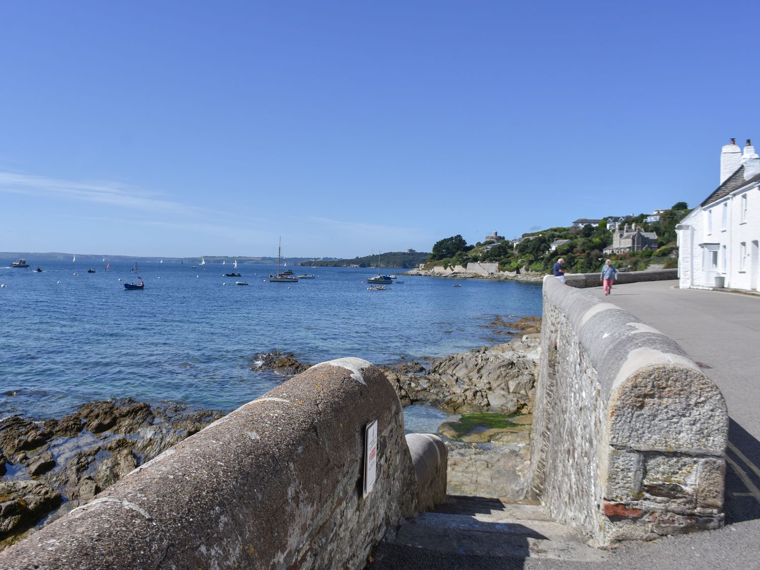 A coastal view with stone steps leading to rocks and water with boats and houses along the shore at Prydes Cottage in St Mawes