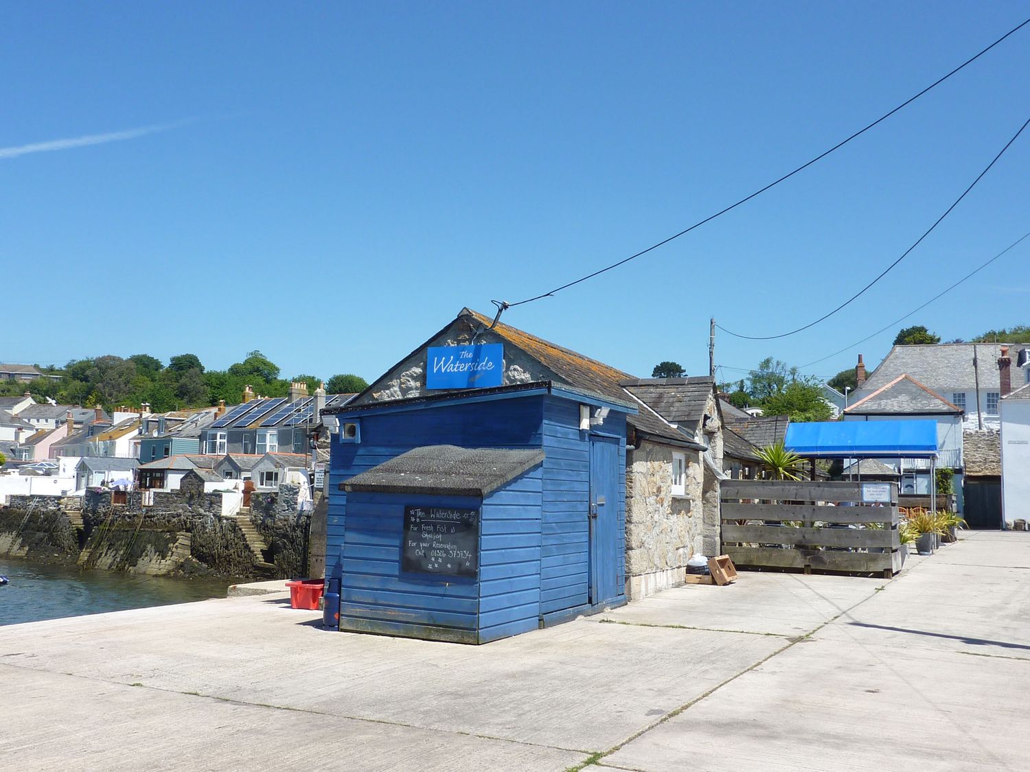 A small blue building with a sign reading The Waterside by a waterfront with houses in the background at Quarry Cottage in Flushing near Falmouth
