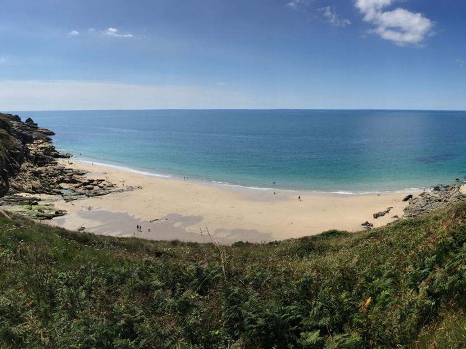 A beach with sand and rocks beside the ocean under a blue sky at The Hayloft in Breage