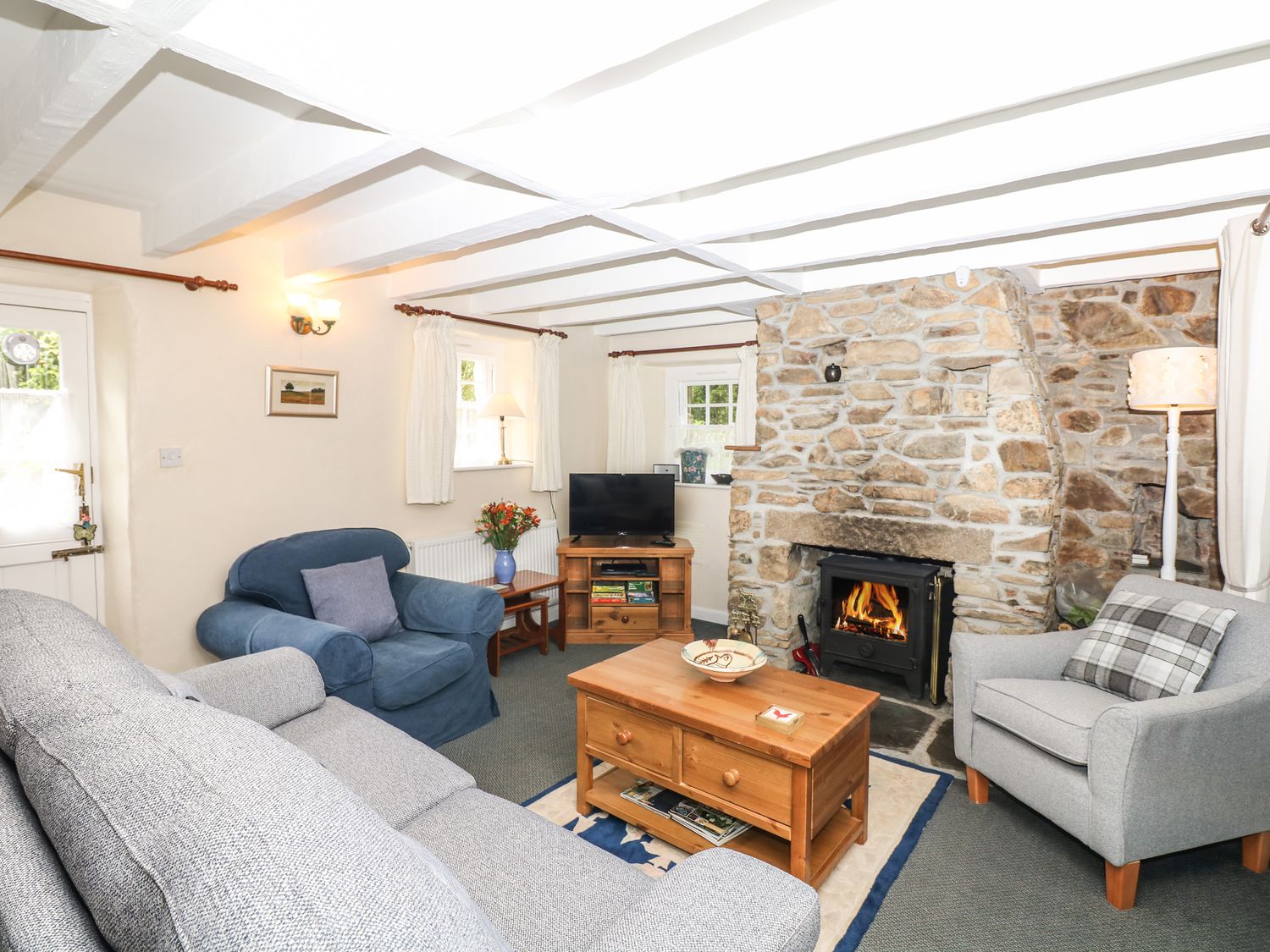 A living room with a stone fireplace a wood burning stove sofas a wooden coffee table and a television at Badger Cottage in Mawgan-in-Meneage near Helston