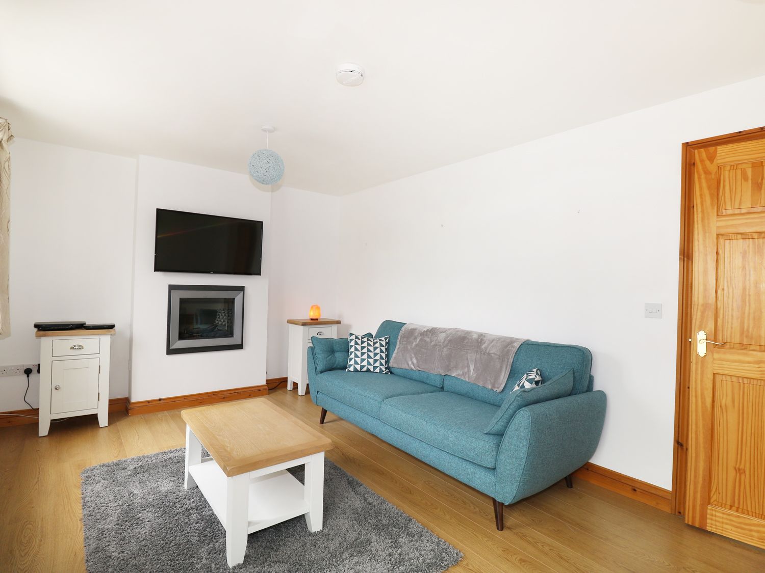 A living room with a blue sofa a wooden coffee table a wall-mounted TV and two white side tables at Jacks Mews in Tintagel