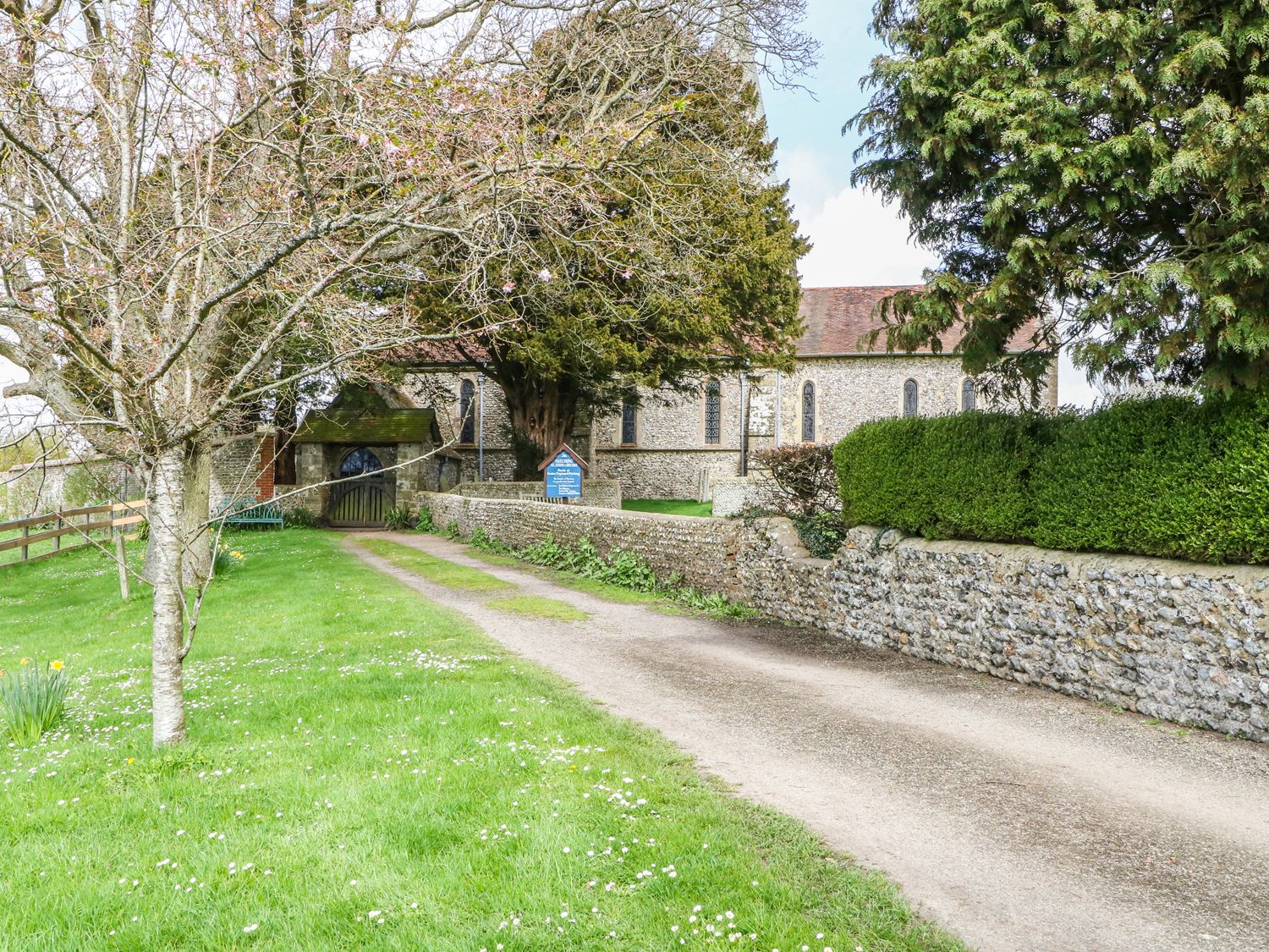 A gravel pathway leading to a stone building with arched windows surrounded by trees and a low stone wall at The Old Dairy in Angmering