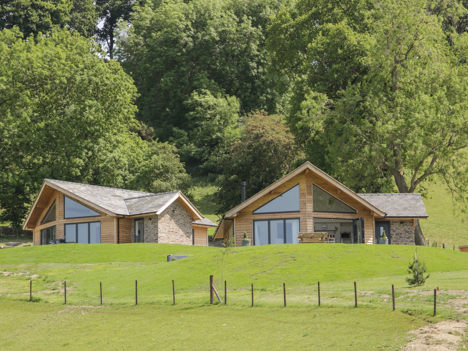 Two wooden and stone houses on a grassy hill with trees in the background at Shepherd's Rest in Montgomery