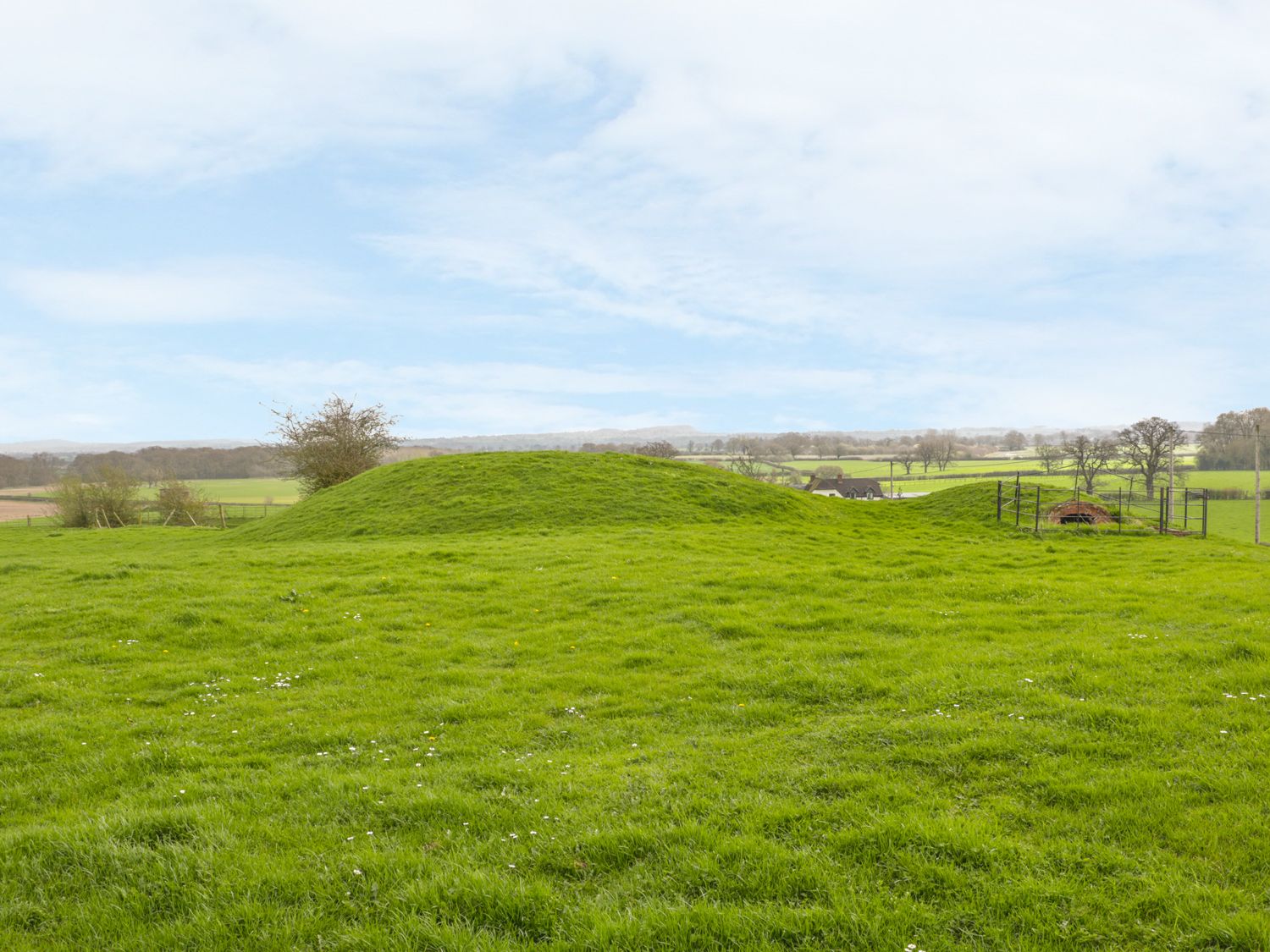 A grassy field with two mounds and a fenced small brick structure in the distance at Acorn Cottage 2 Burlton near Ellesmere