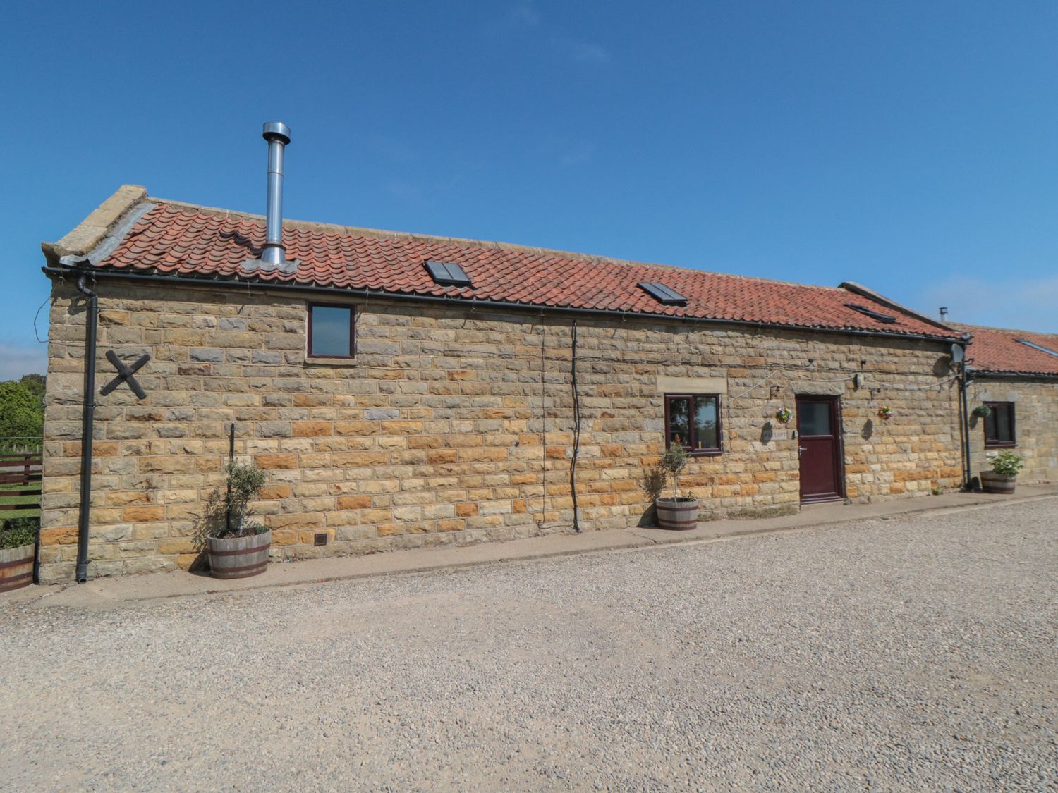 An exterior view of a building with a stone wall and a gravel driveway at Hayloft in Staintondale