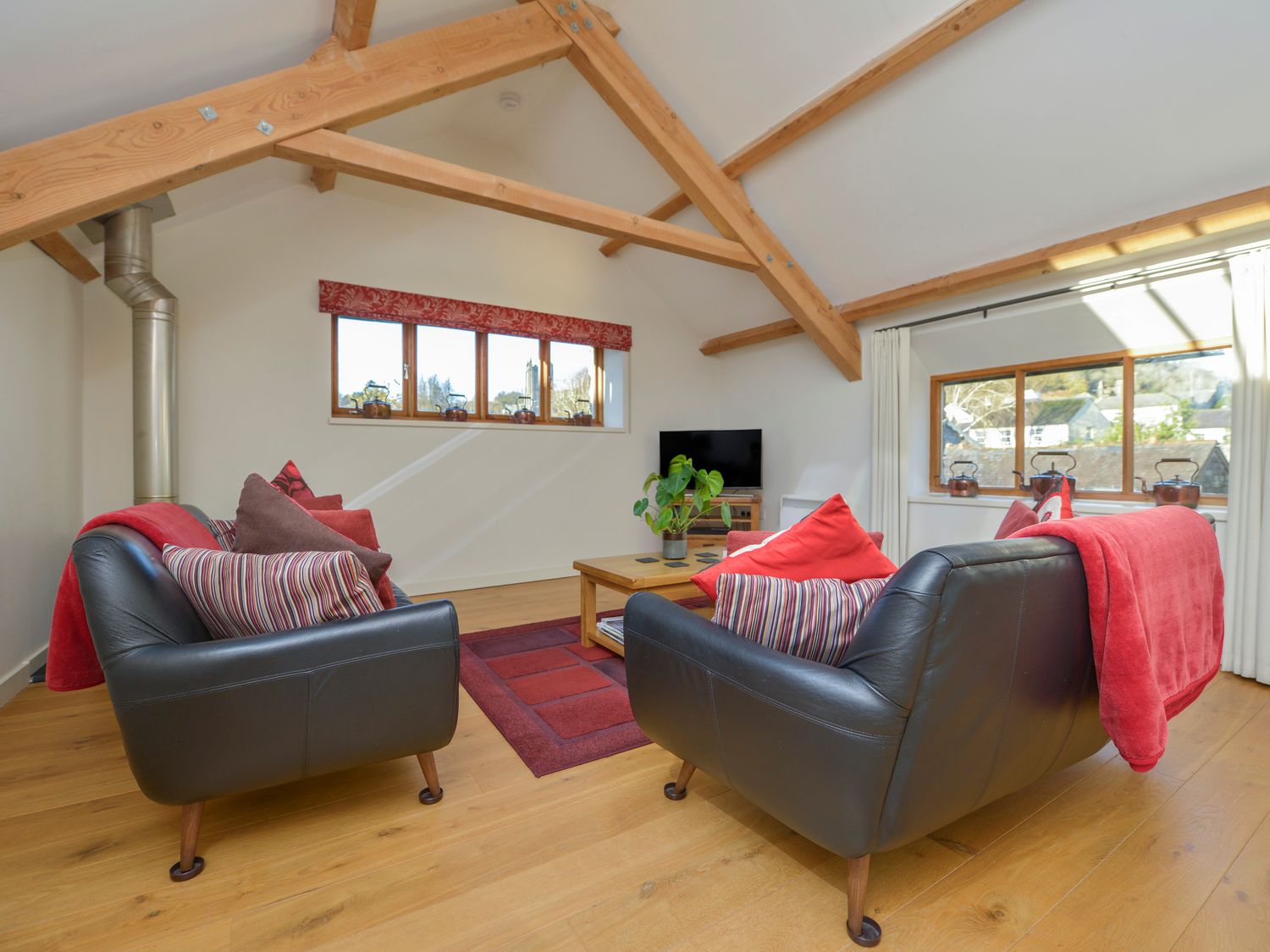 A living room with two black leather sofas and wooden beams at Old Armoury Barn Ashburton