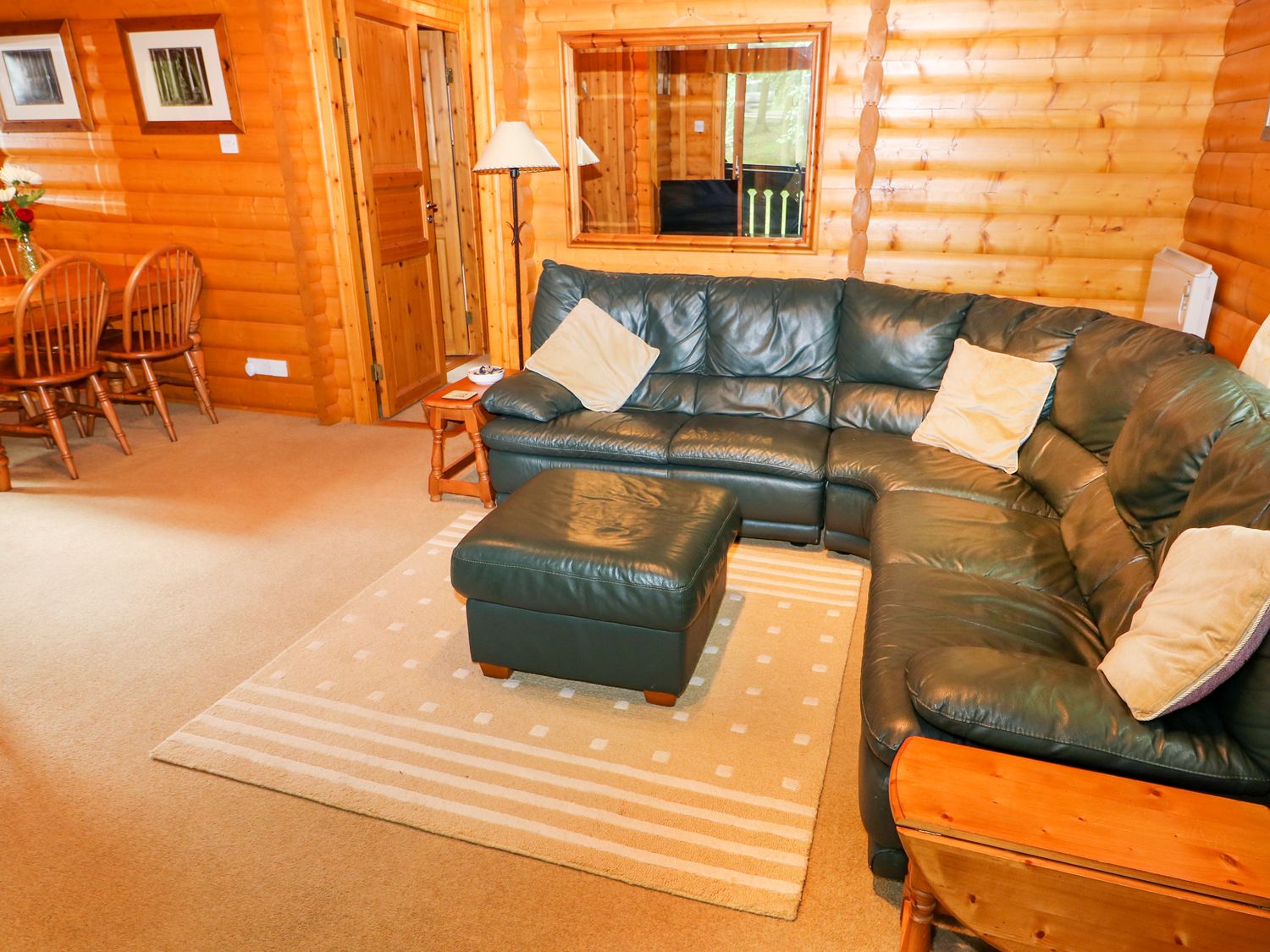 A living room with a green leather corner sofa and ottoman with a wooden dining table and chairs in Lodge 8 in Louth