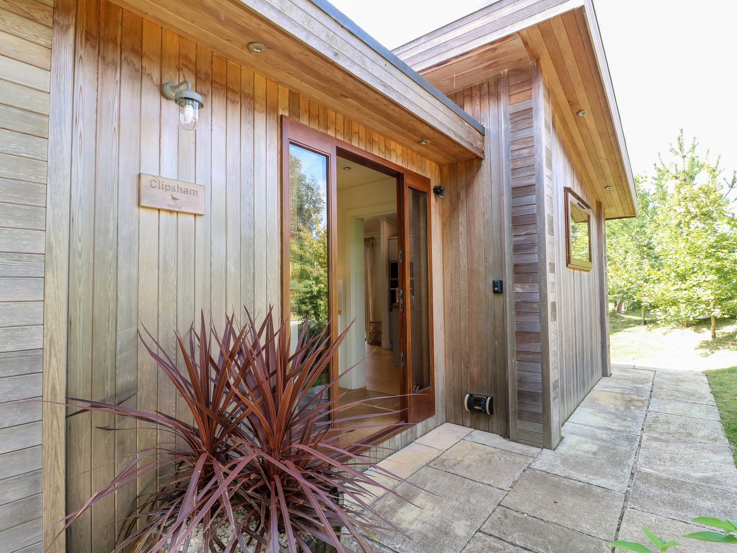 The entrance of a wooden house with a glass door a plant outside and a sign that says Clipsham at Clipsham Exton Rutland