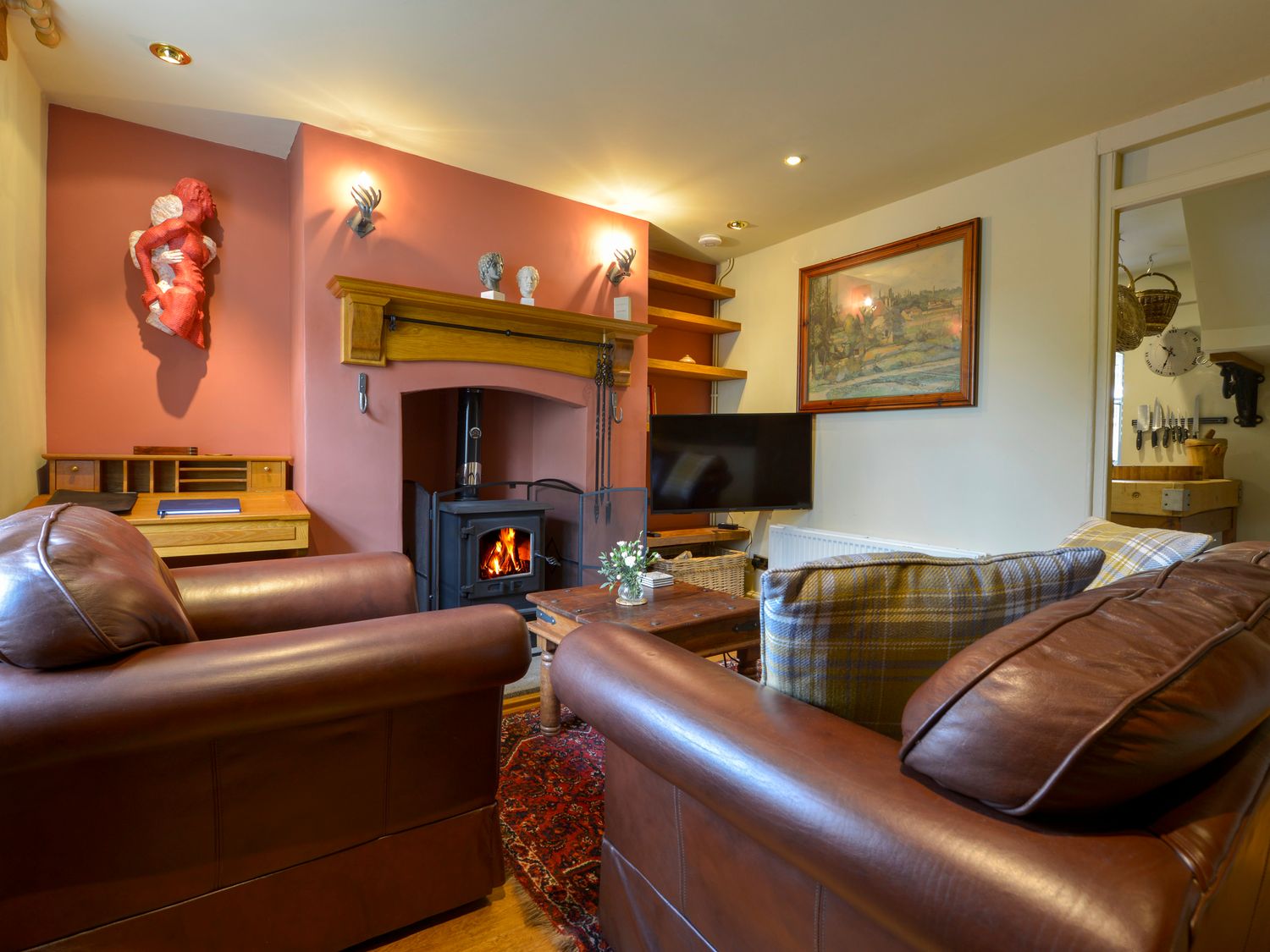 A living room with two leather sofas a wood burning stove and a television at 11 The Village in Yelverton