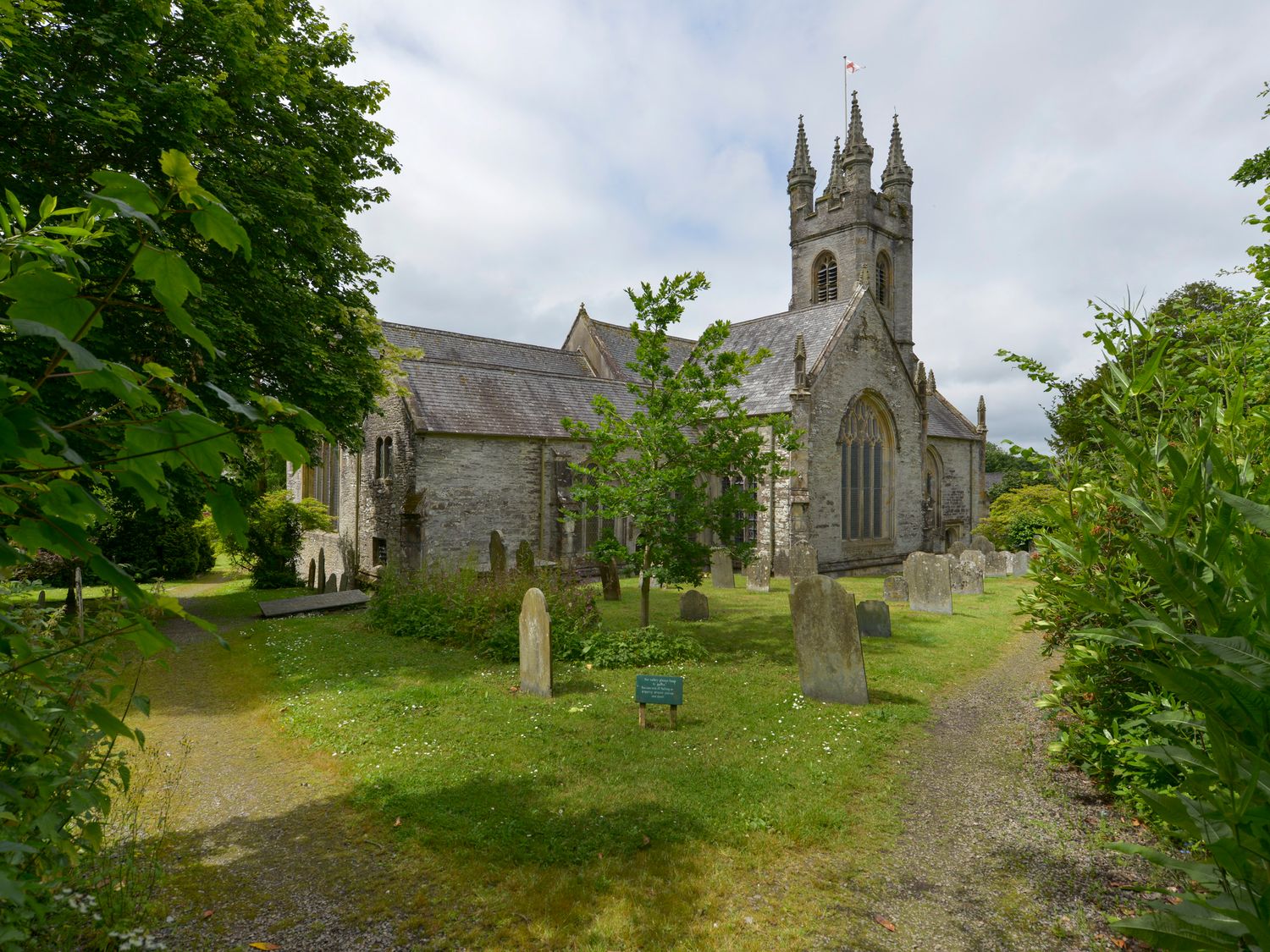 An old stone church with a tower surrounded by gravestones and greenery at 11 The Village in Yelverton