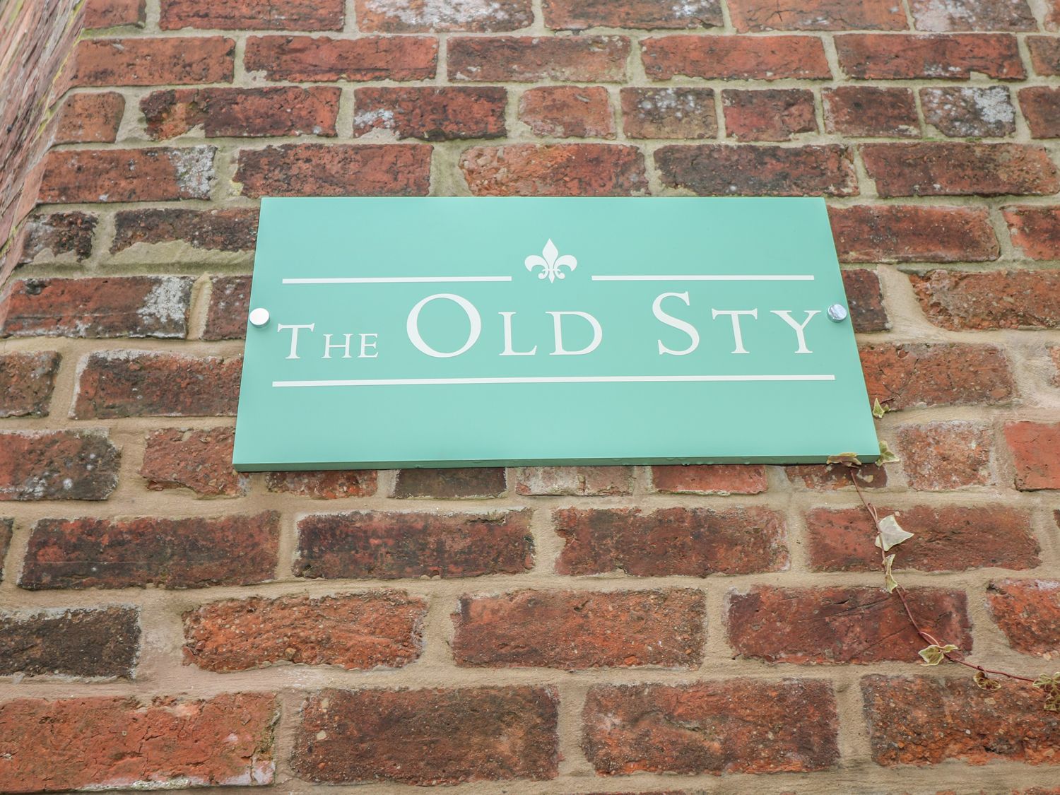 A green sign with the text The Old Sty mounted on a brick wall at The Old Sty in Alton