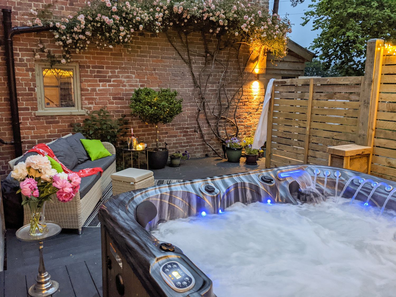 An outdoor seating area with a hot tub flowers and a sofa on a patio at The Dovecote in Craven Arms