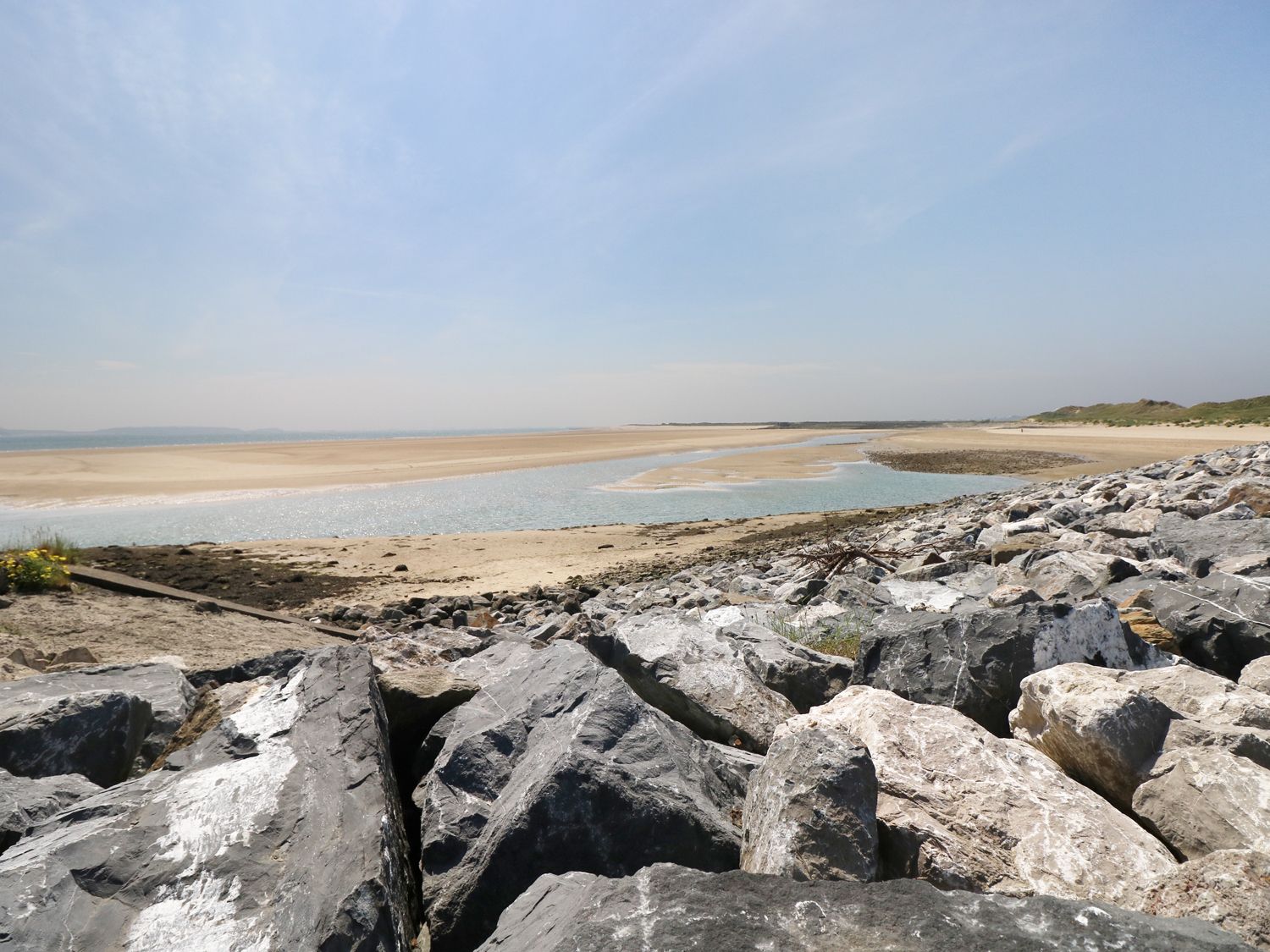 A rocky shoreline with a sandy beach and water under a blue sky at 5 Chandlers Yard in Burry Port