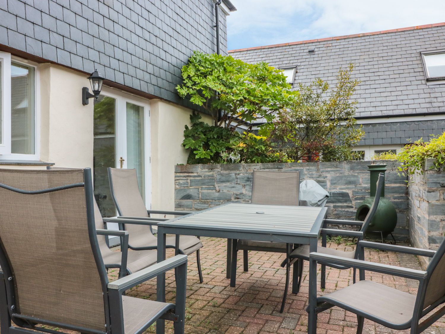 An outdoor patio with a square table and six chairs surrounded by stone walls and plants at Sorrel Cottage in Padstow