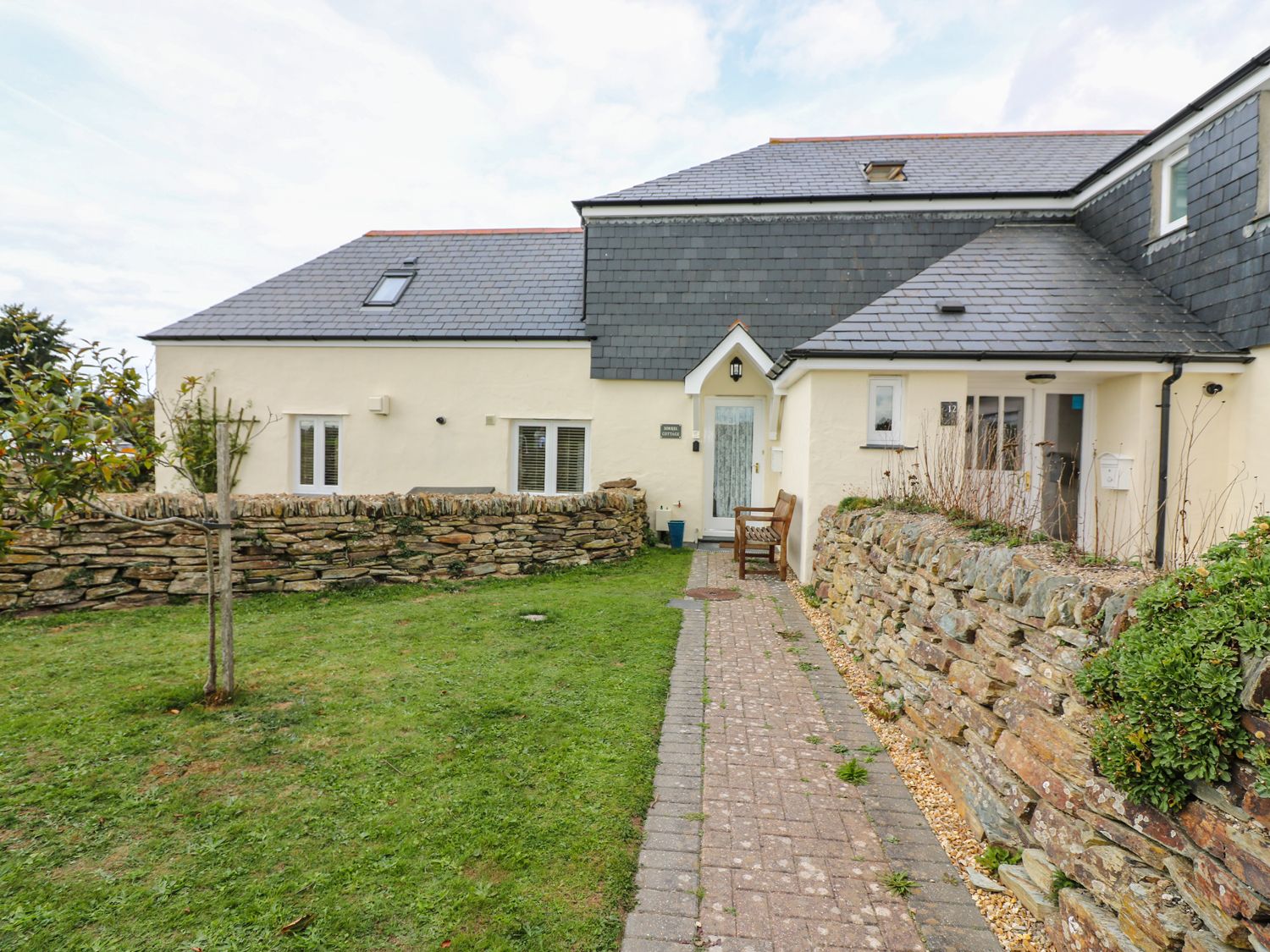 A house with beige walls a slate roof a stone wall and a grass lawn at Sorrel Cottage in Padstow
