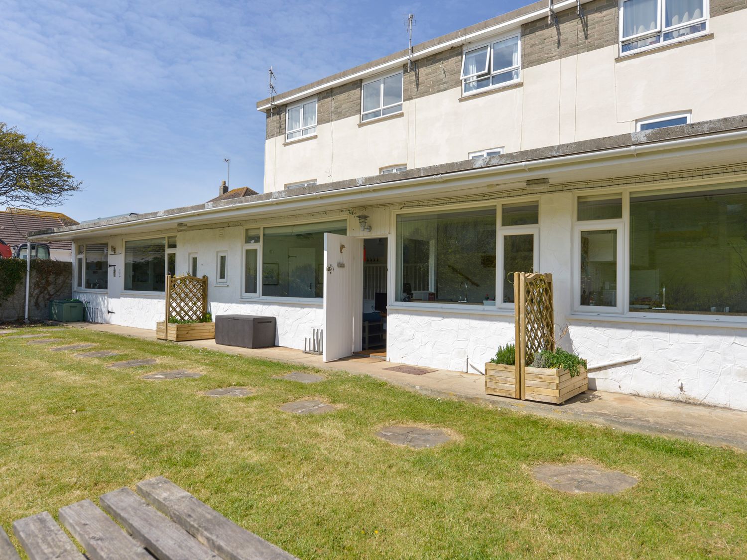 A garden area with a grass lawn and stepping stones in front of a white building with windows and an open door at 2 Brook Cottages in Hope Cove