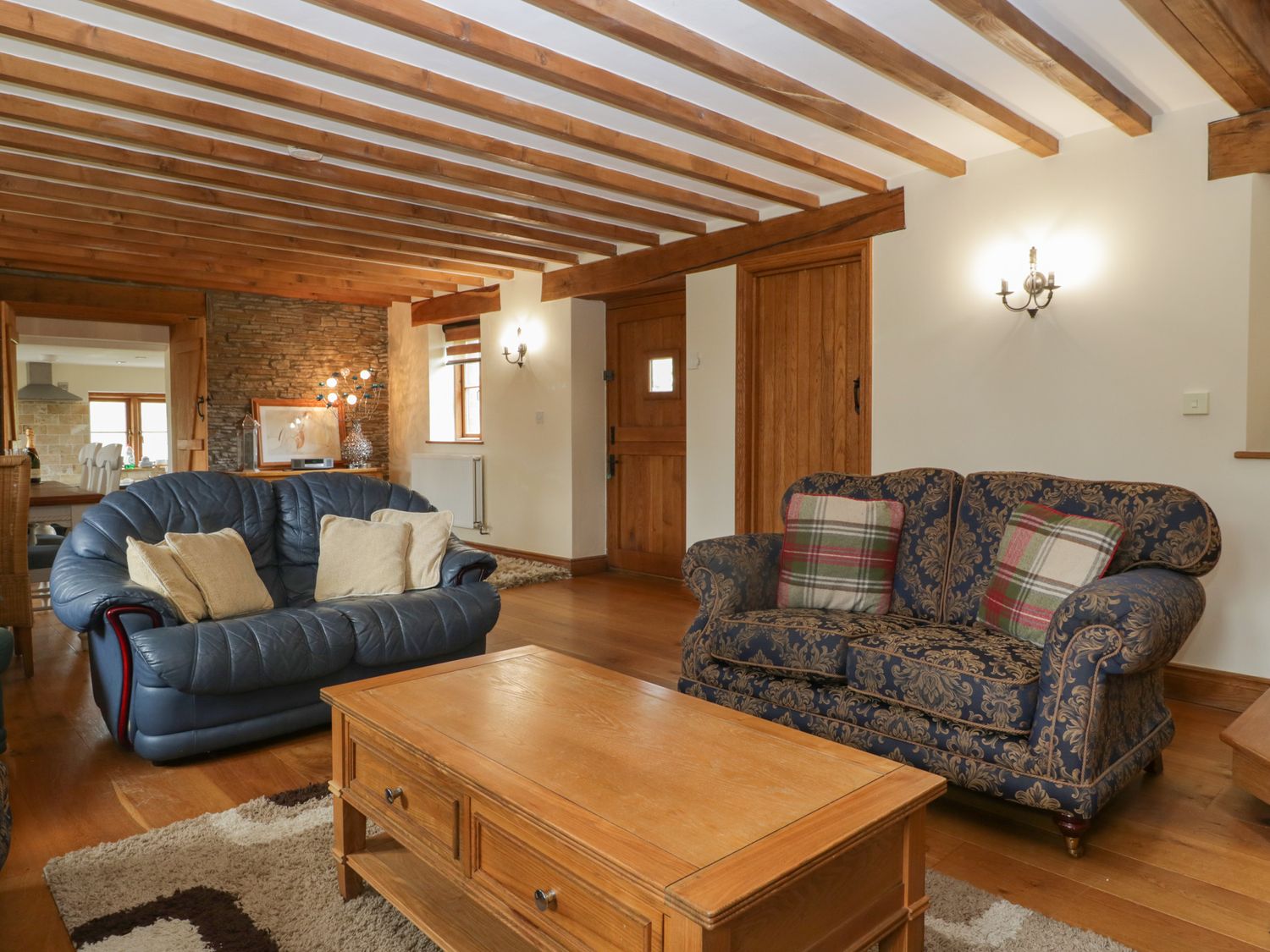 A living room with two sofas a wooden coffee table exposed wooden ceiling beams and a stone wall at Penrhiwarwydd Barn in Pontywaun