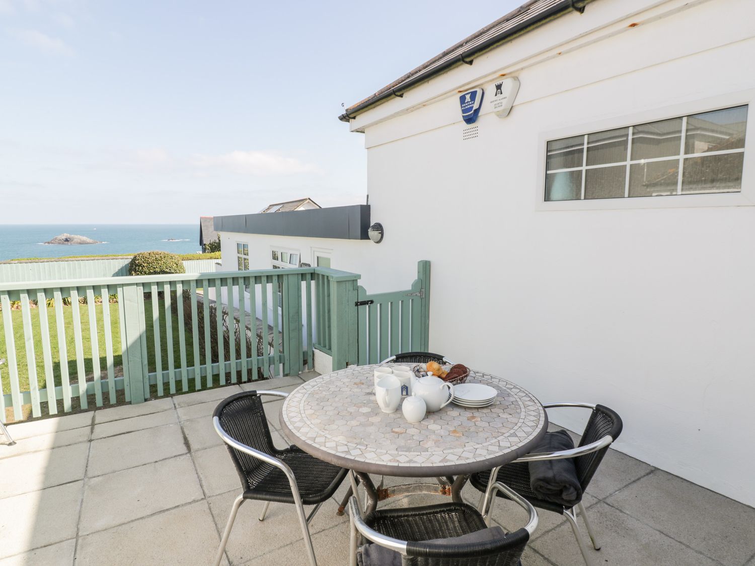 An outdoor patio with a round table set with dishes and chairs overlooking the sea at Guillemot in Crantock