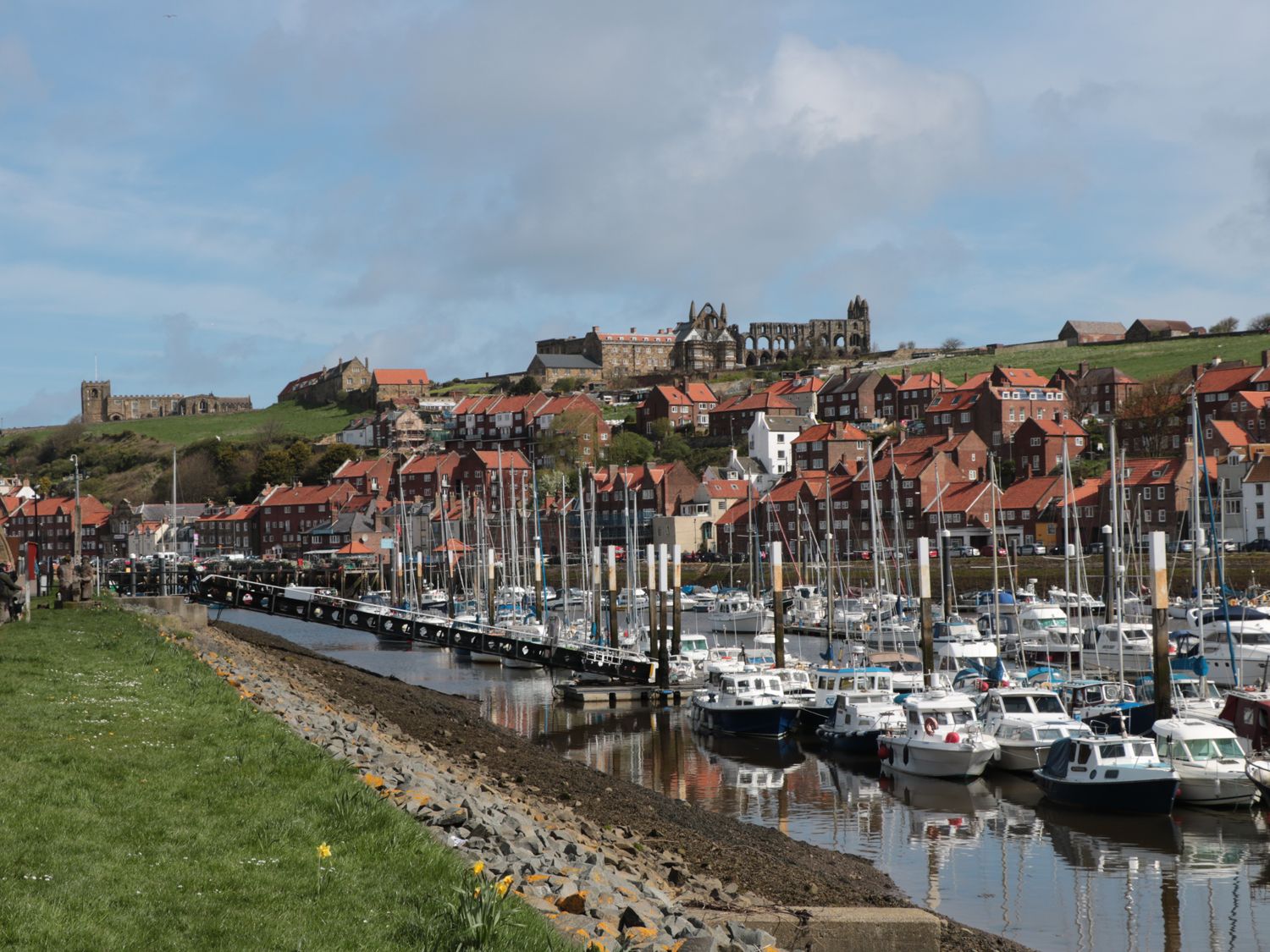 A marina with boats docked along the water and houses on a hillside with an abbey in the background at 11A Church Street in Whitby