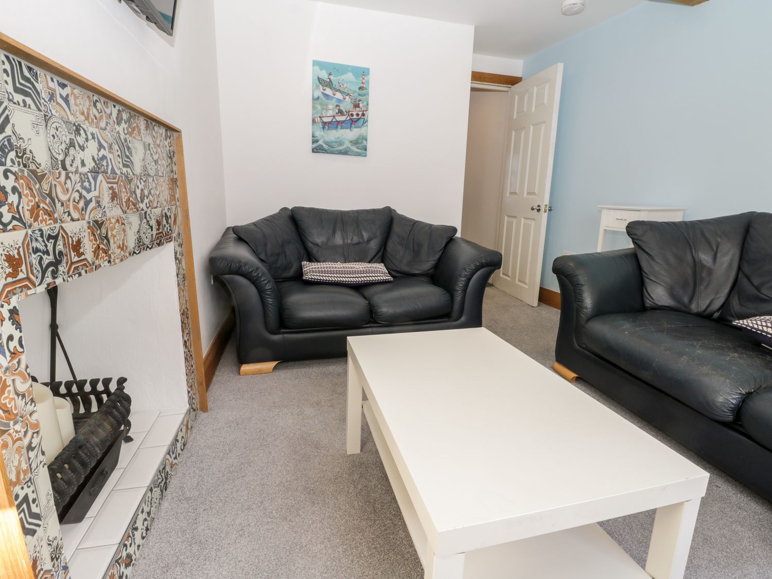 A living room with black sofas white coffee table and a tiled fireplace at 11A Church Street Whitby