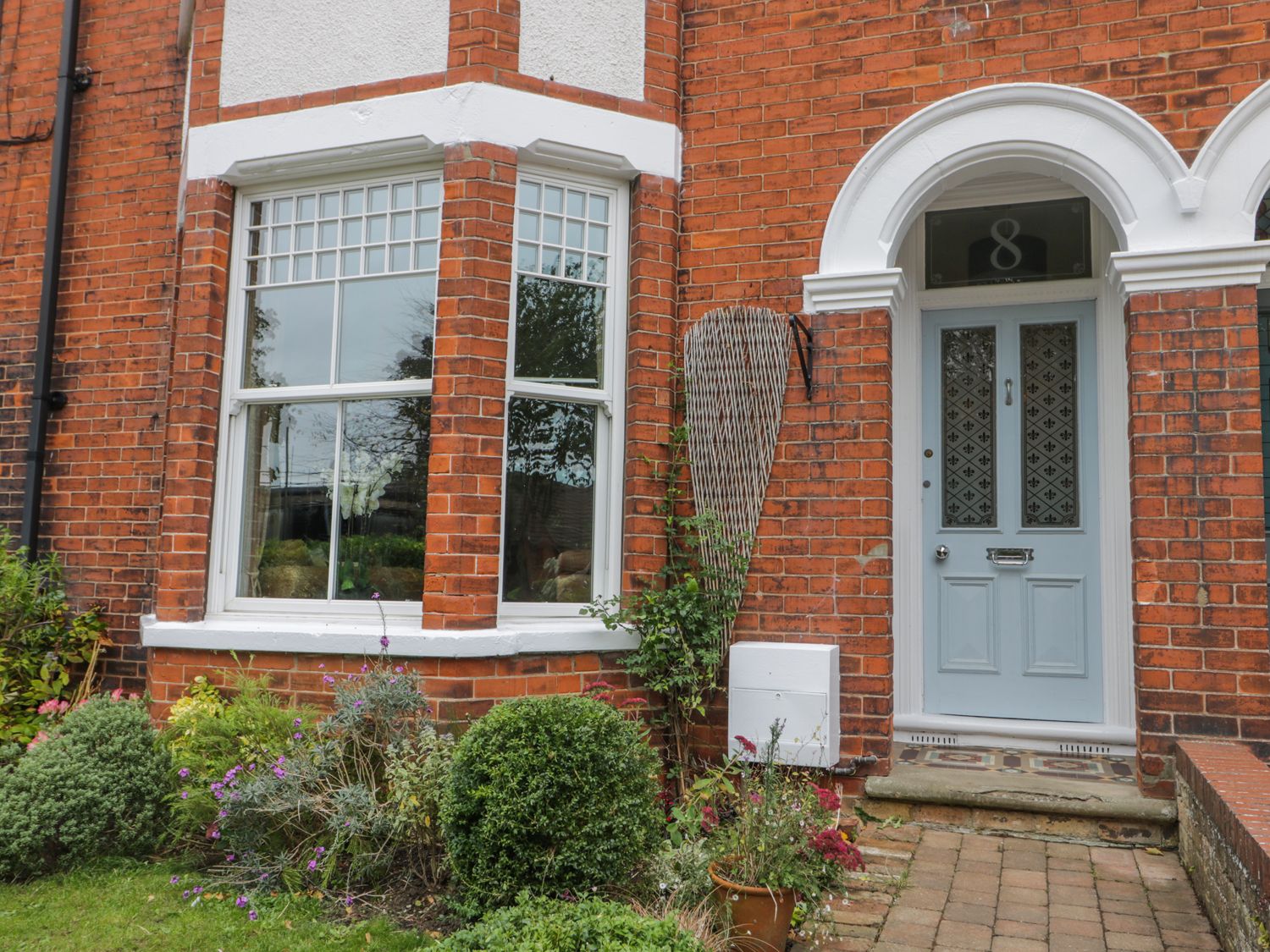 A brick house front with a grey door numbered 8 and a bay window with plants in front at 8 Wilton Road in Hornsea