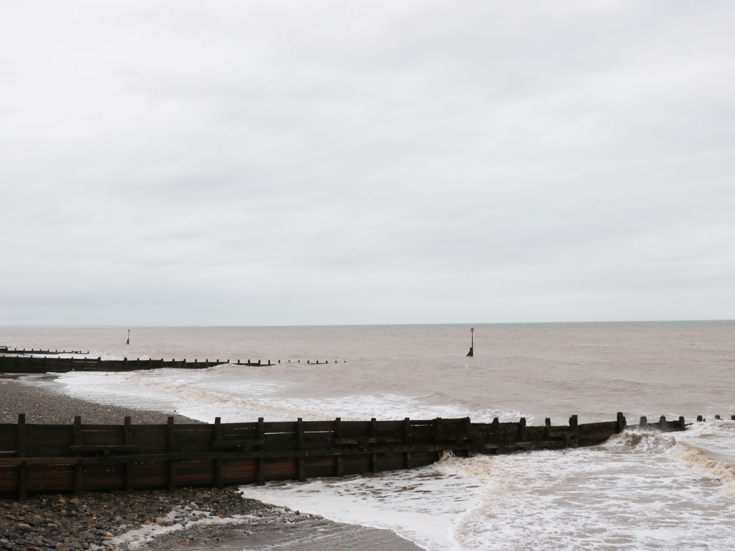 A coastal scene with wooden groynes extending into the sea and waves breaking on a pebbly shore at 8 Wilton Road in Hornsea