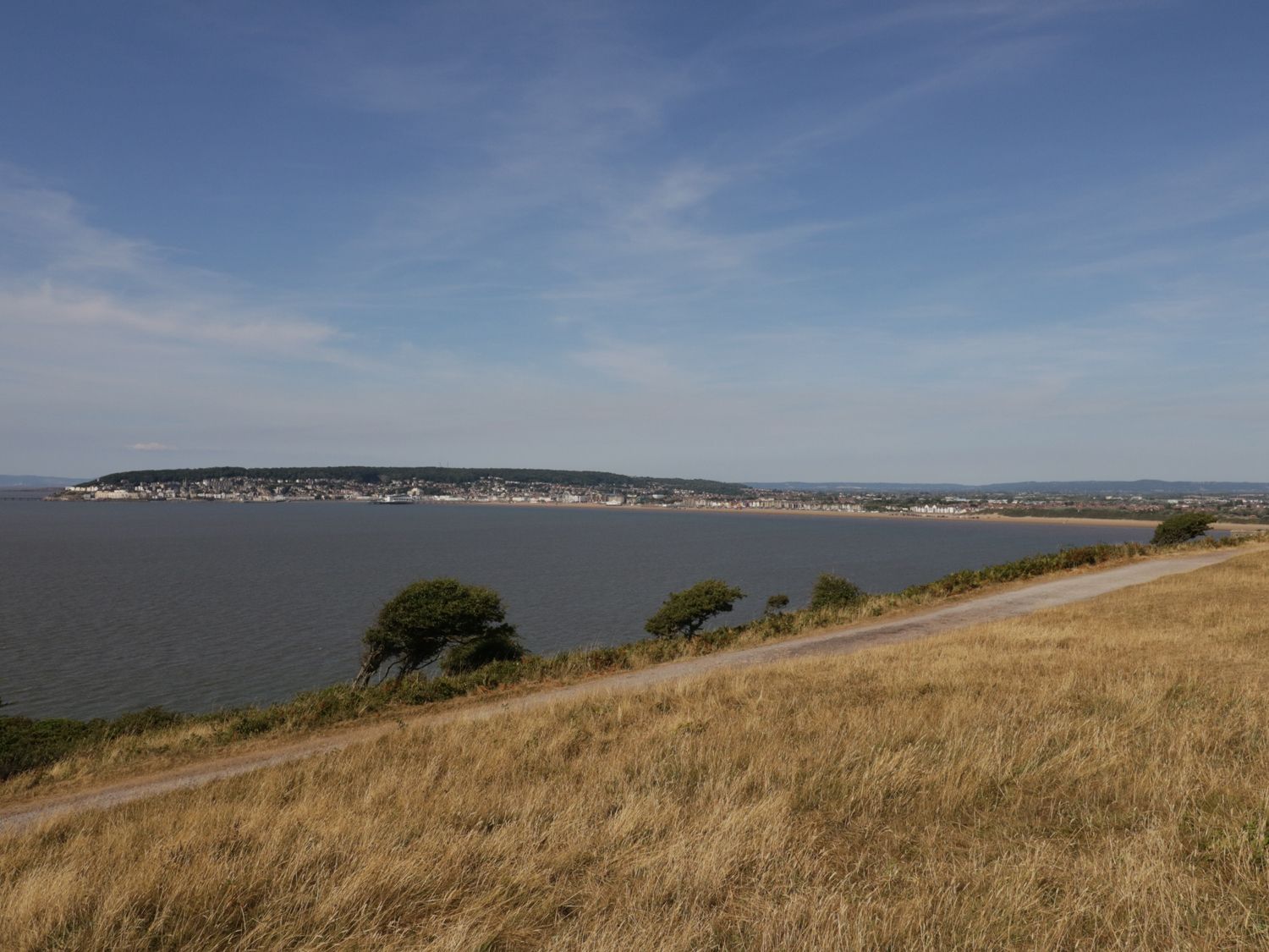 A coastal landscape with a pathway running alongside dry grass and trees overlooking a bay with a town in the distance at Ocean Breeze in Brean