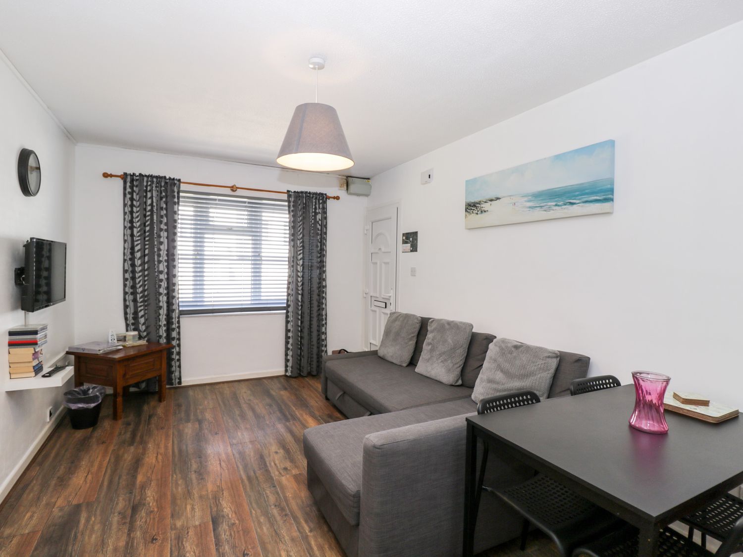 A living room with a gray sofa and table with chairs next to it and a small wooden side table with books on it Ocean Breeze Brean