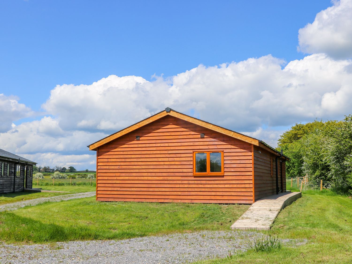 A wooden cabin with a single window and a concrete pathway surrounded by grass at Oak Lodge in Sheriff Hutton