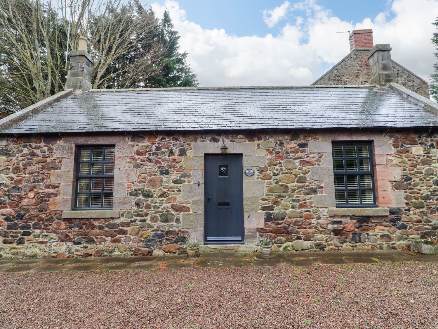 A stone cottage with two windows and a dark door in the center at Bracken Lodge in Wooler