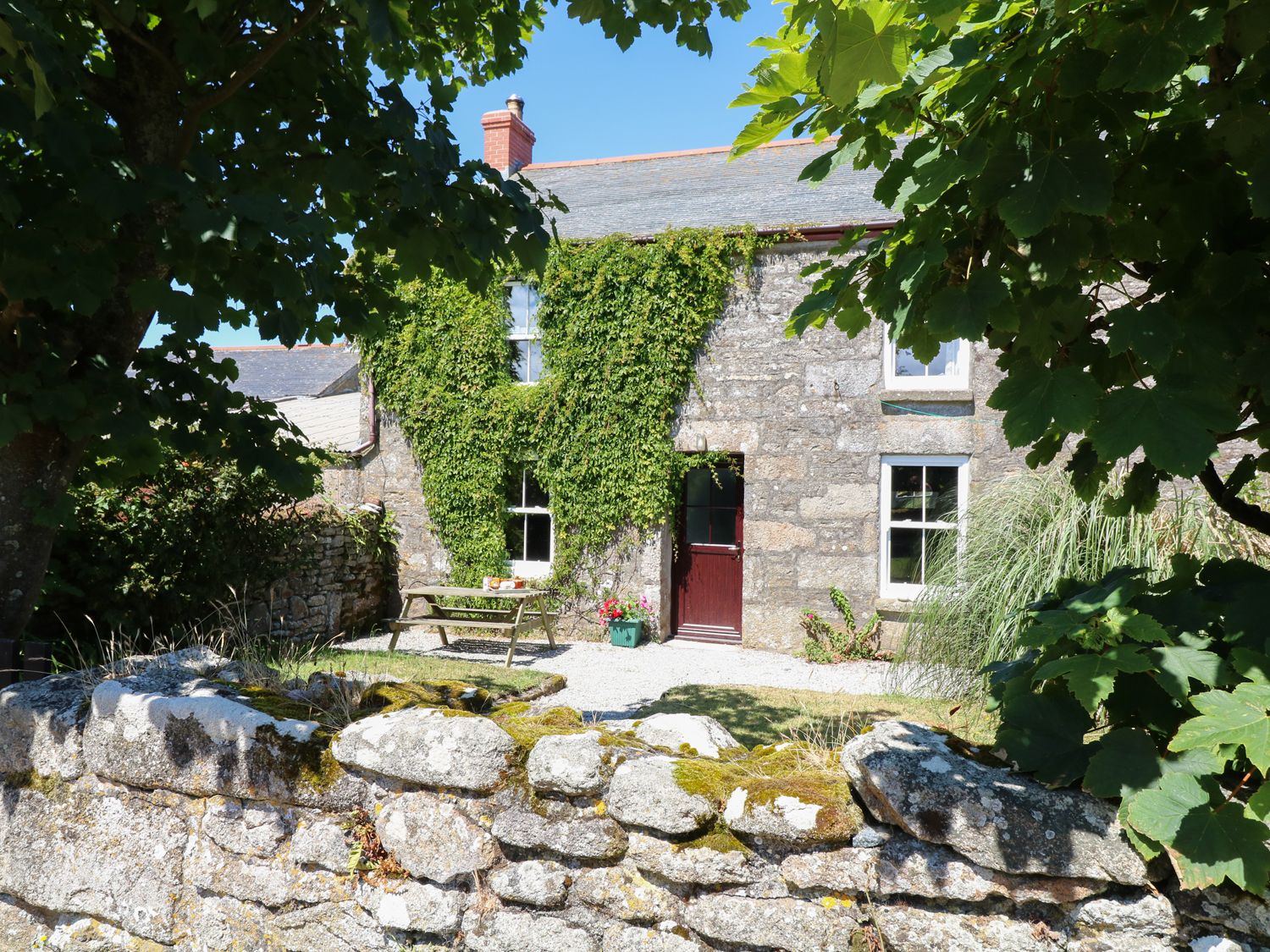 A stone cottage with ivy on the wall picnic table and stone wall in front at The Farmhouse in Pendeen