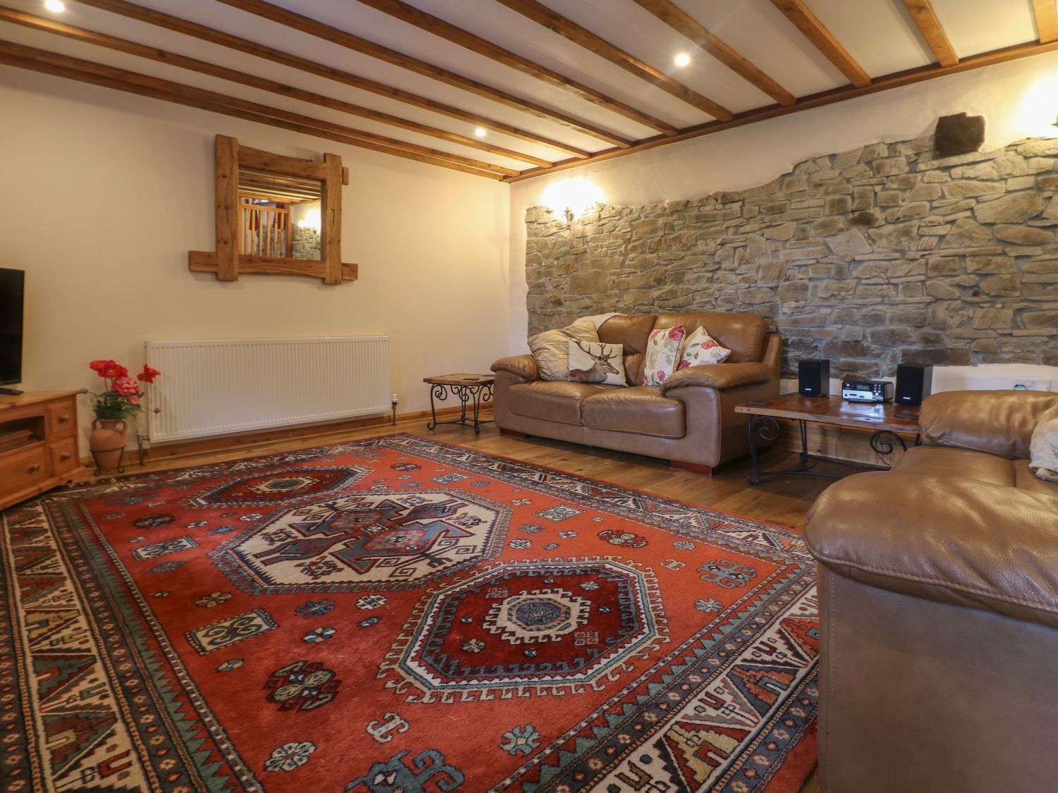 A living room with leather sofas a red patterned rug and a stone wall at Post House in Holsworthy