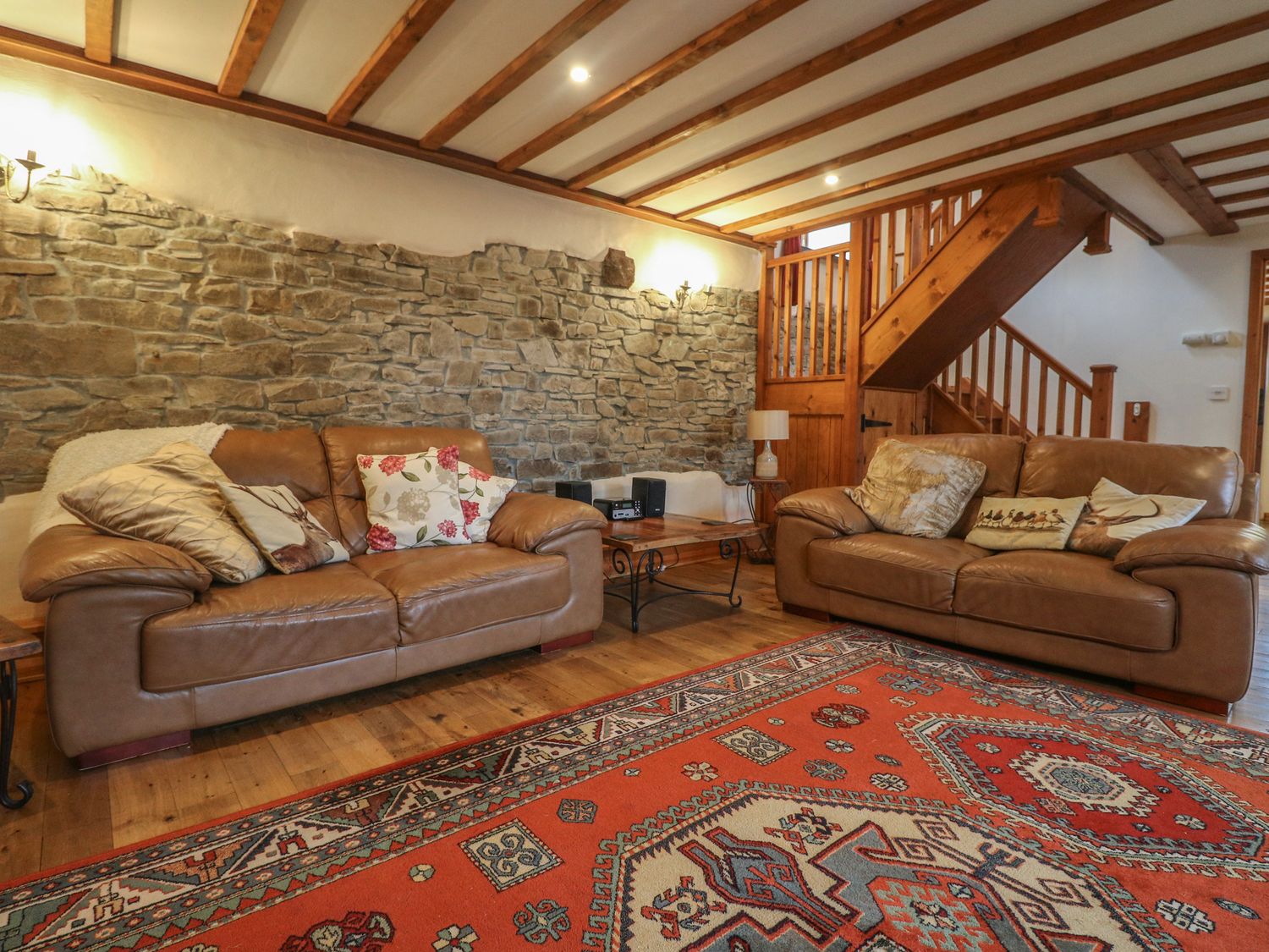 A living room with two leather sofas a wooden coffee table and a red patterned rug at Post House in Holsworthy