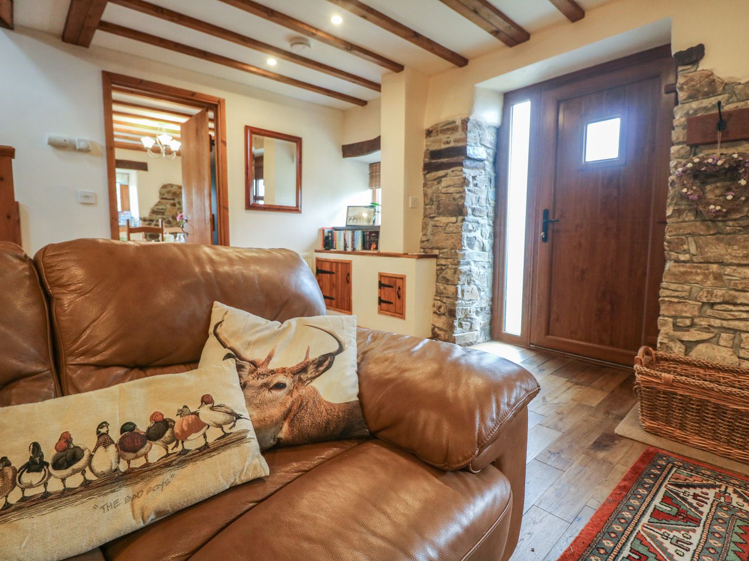 An entryway with a wooden front door stone walls a brown leather sofa with animal print cushions and a wooden floor at Post House in Holsworthy