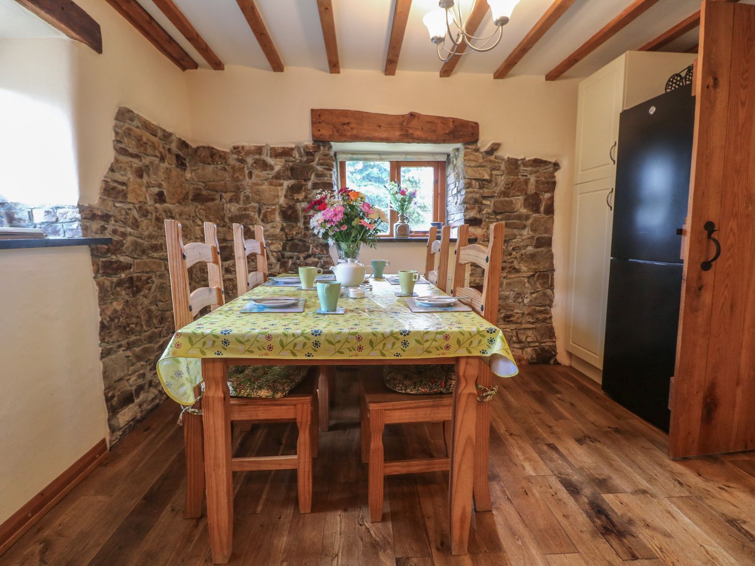 A dining room with a wooden table and chairs a yellow tablecloth and a flower vase on the table at Post House in Holsworthy