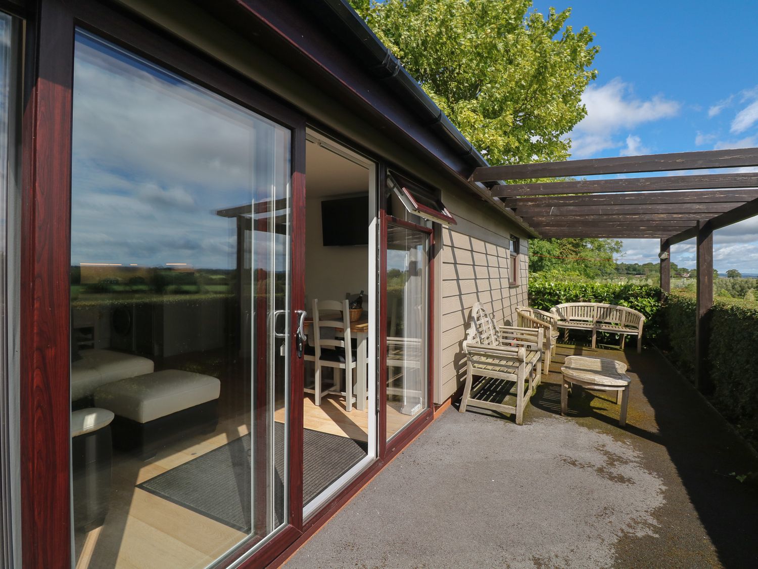A patio with wooden chairs and a table outside a building with glass sliding doors at Upham View in Woodbury