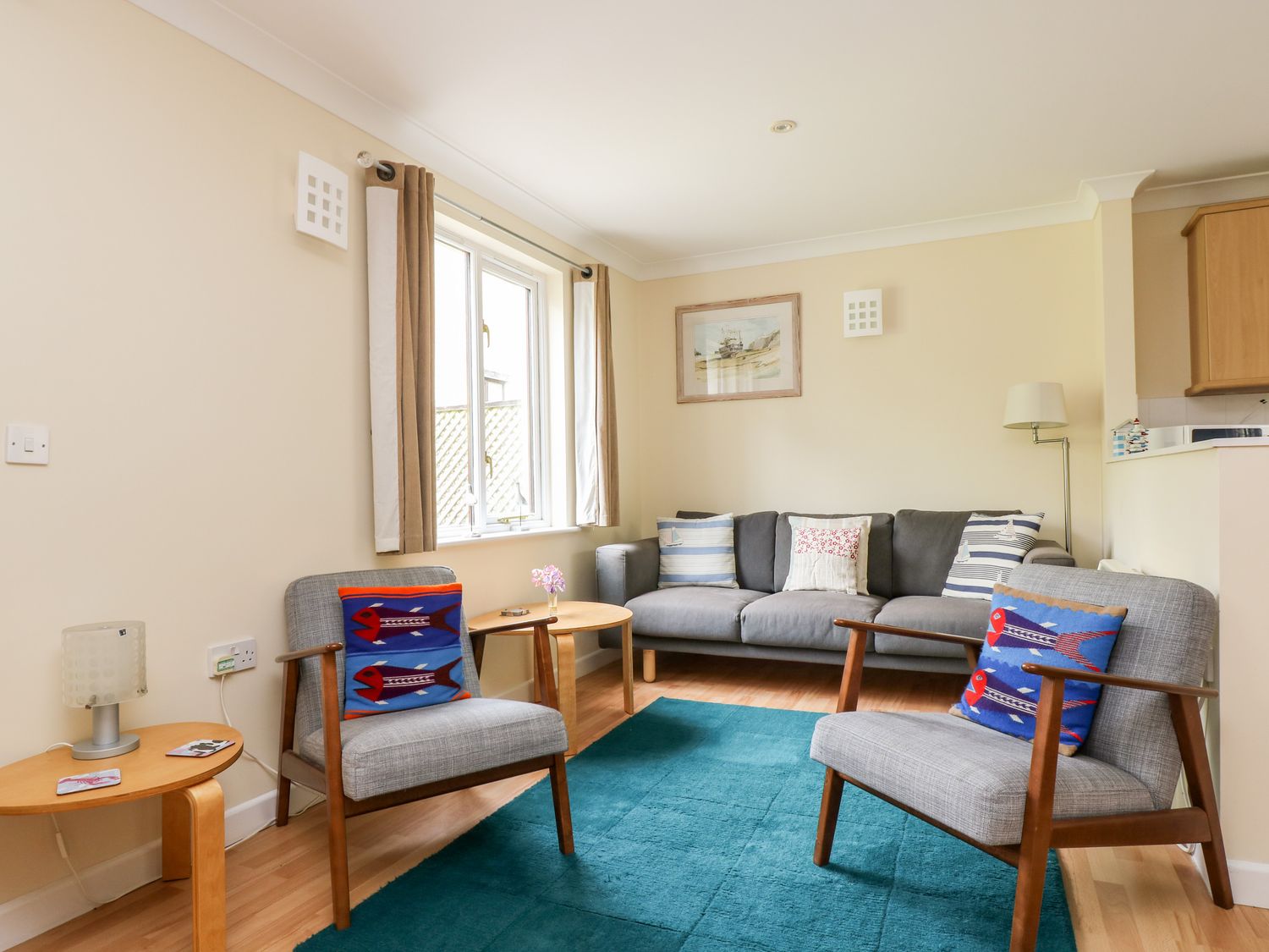 A living room with two chairs, a sofa, a blue rug, wooden side tables, and a window with curtains at Pugwash Cottage in Falmouth