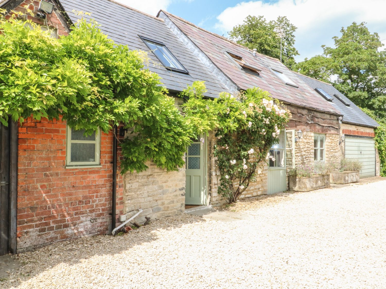 Exterior view of a stone and brick cottage with green doors and climbing plants on the walls at Somerford Cottage in Malmesbury