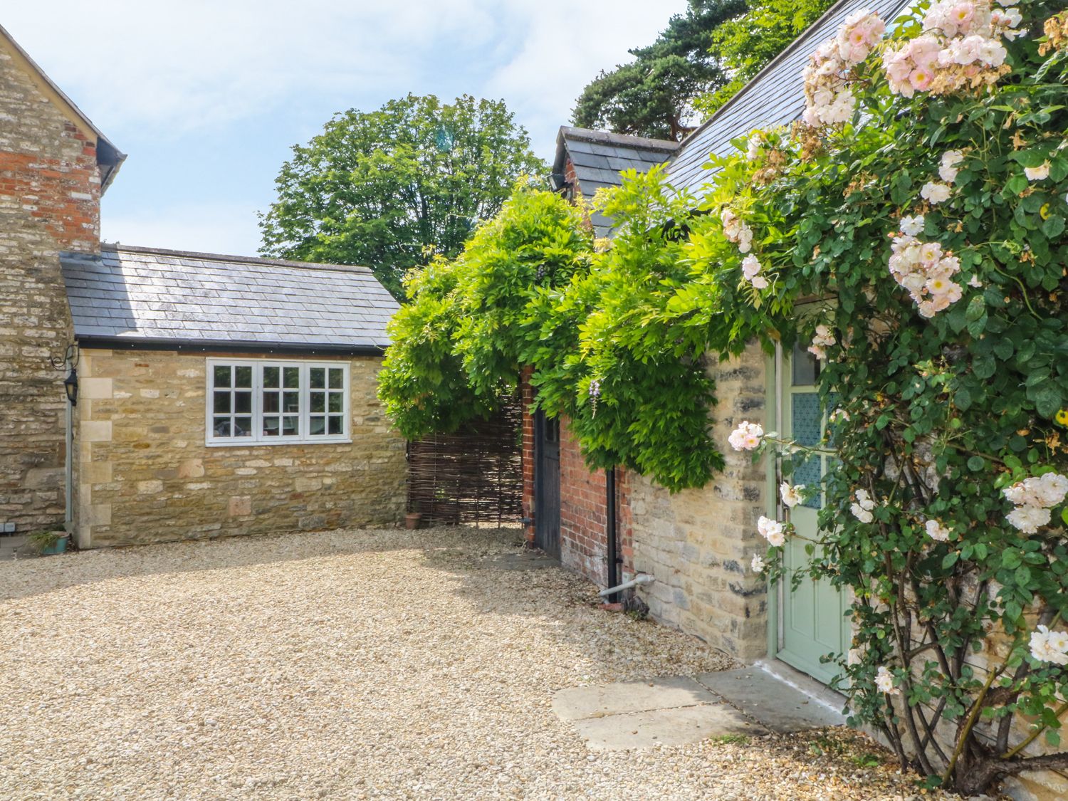A stone and brick exterior with a light green door and climbing plants at Somerford Cottage in Malmesbury