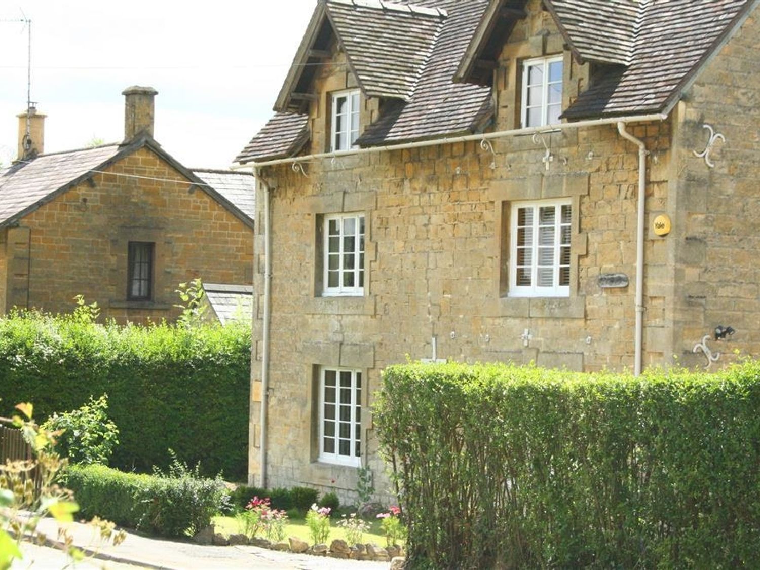 A stone house with white windows and a hedge in front at Elm View in Chipping Campden