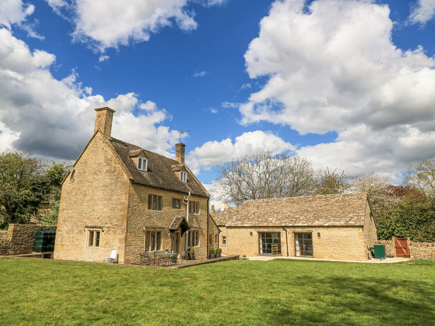 A stone house and an adjoining single-story building with a lawn and trees at The Smithy in Broadwell