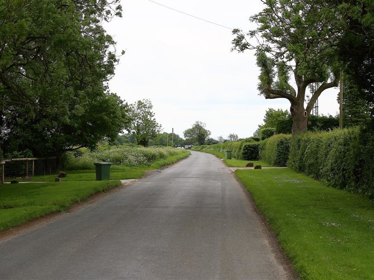 A country road lined with trees green hedges and green trash bins at Park Stables Wyck Beacon near Bourton-on-the-Water