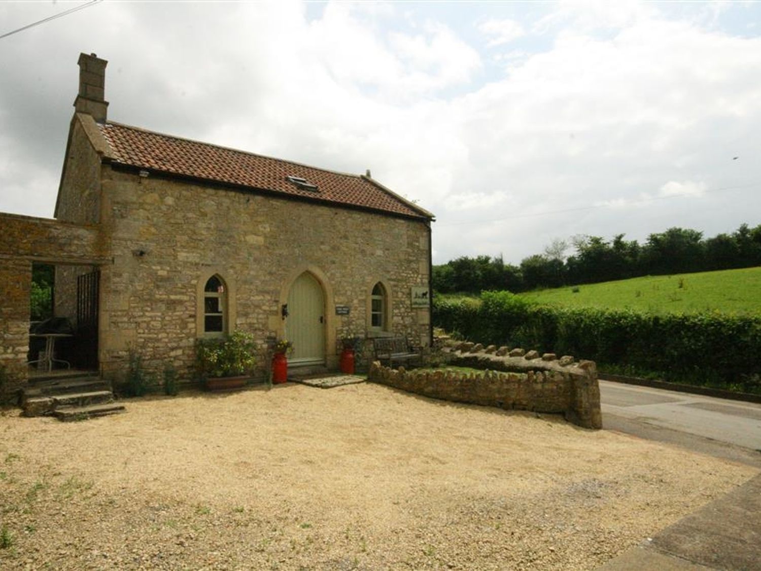 A stone cottage with a tiled roof and arched door in a rural area at Cider Press Cottage in Priston Village Bath