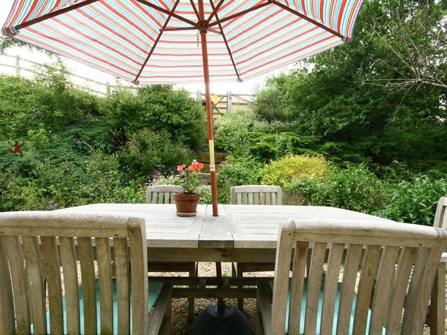 An outdoor wooden table and chairs with a striped umbrella and a potted plant in a garden at Cider Press Cottage Priston Village Bath