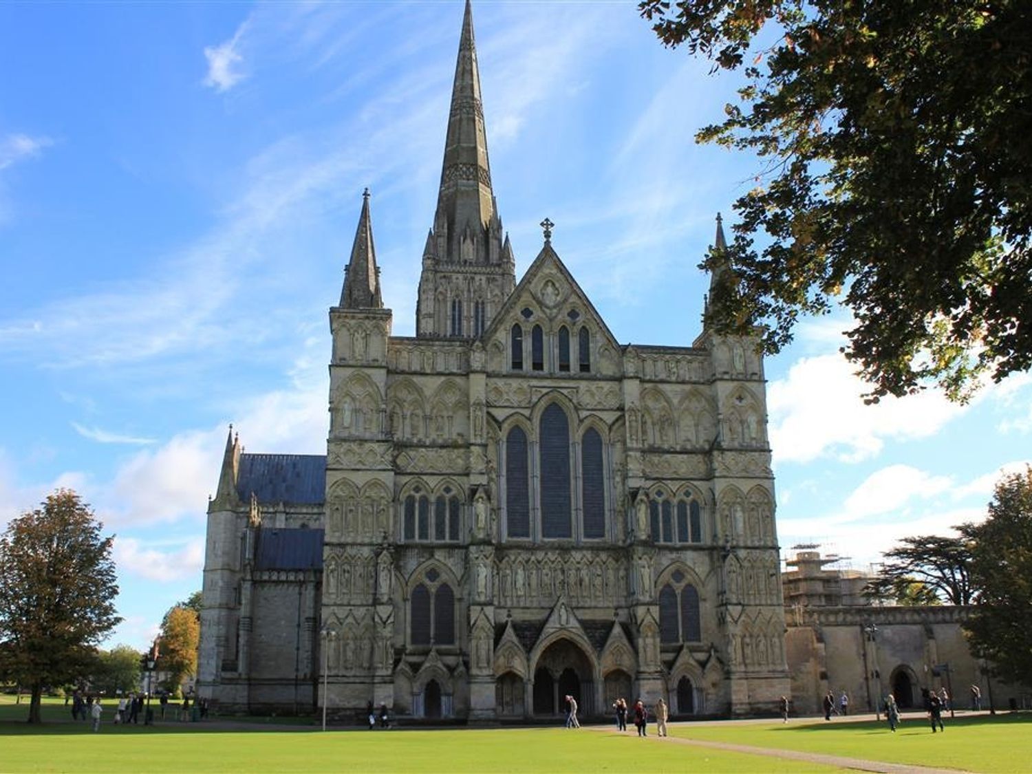 A large cathedral with tall spires and arched windows surrounded by a grassy area and trees at Rojoy in Salisbury