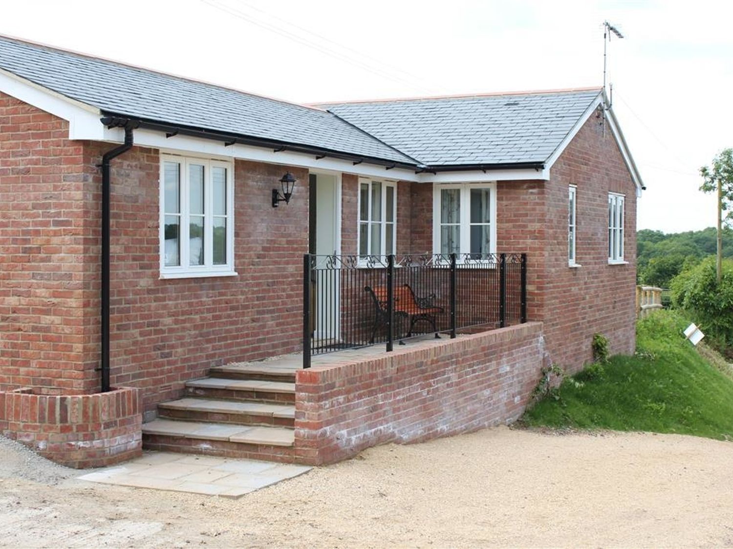 A brick house with white framed windows a small porch with black railing and two chairs at The Tractor Shed in Salisbury
