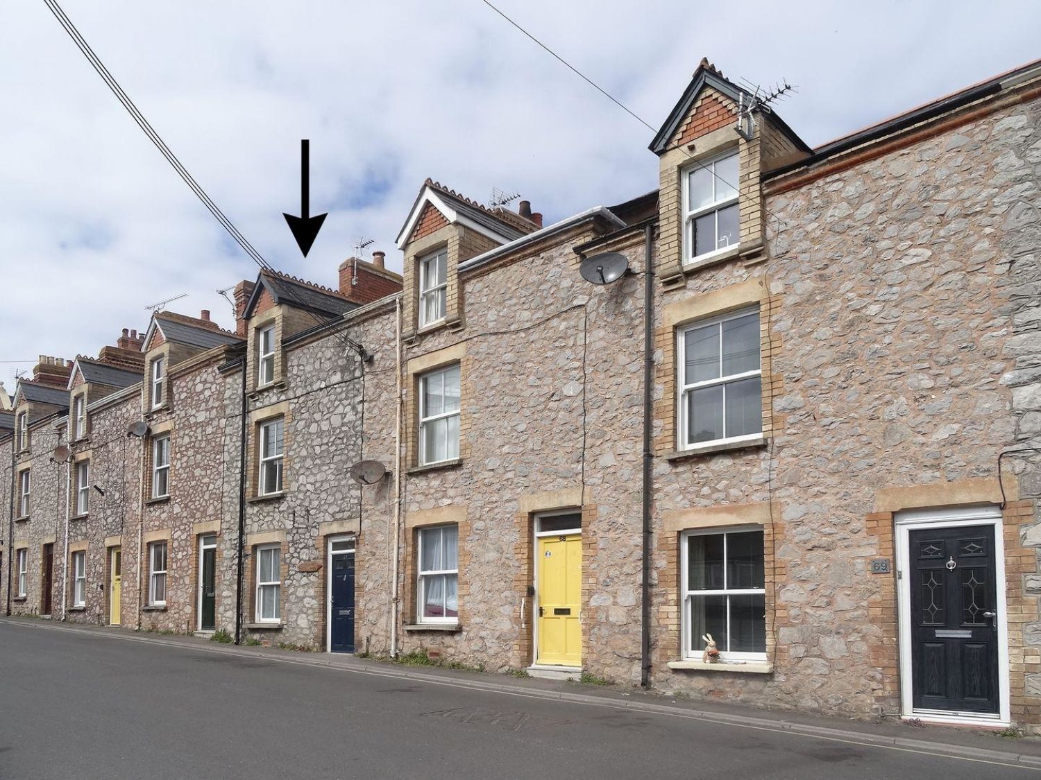 A row of stone terraced houses with various colored doors along a street with an arrow pointing to one house at Anchorage Watchet
